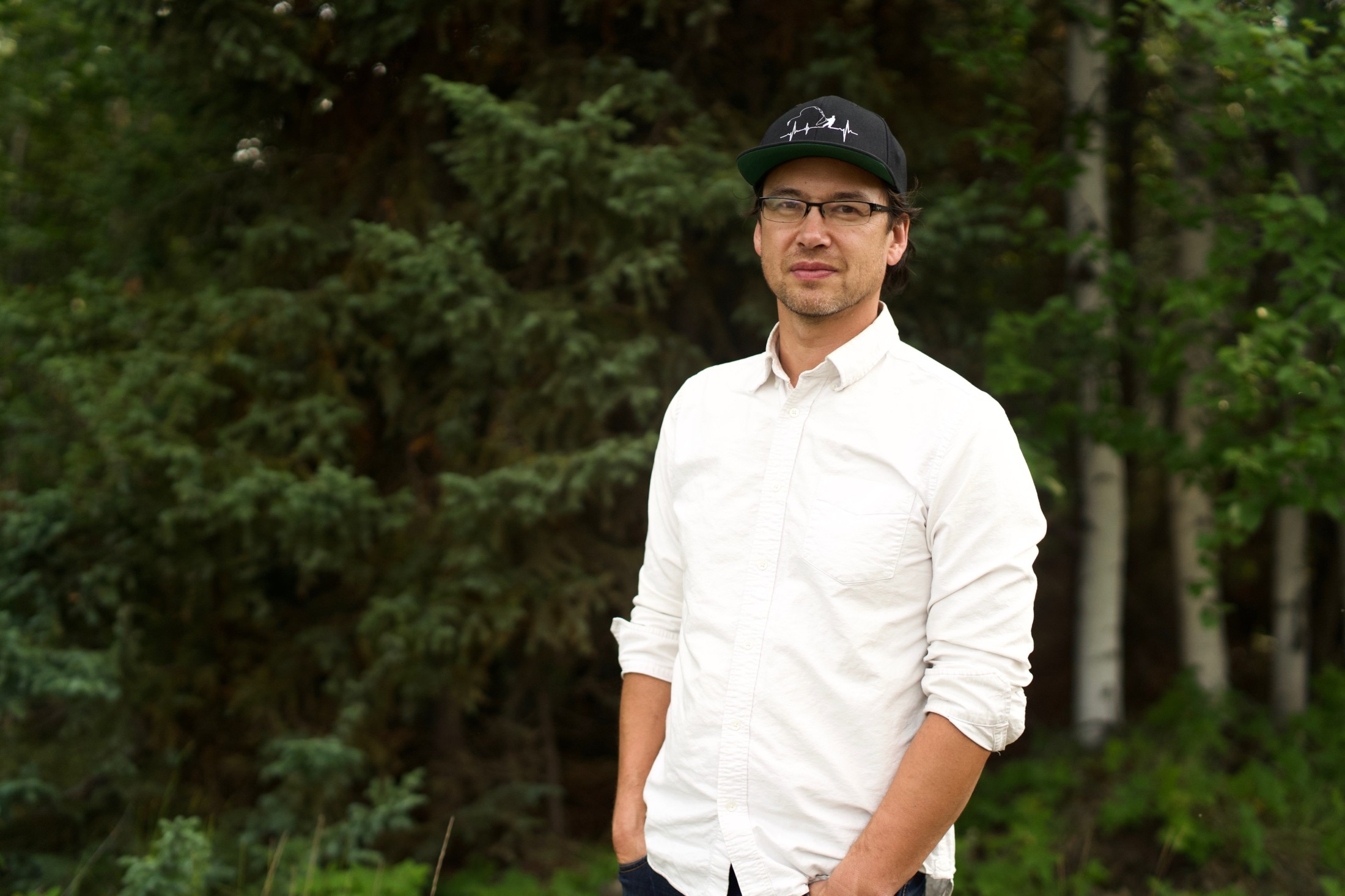Steve Ellis, a negotiator for Lutsel K’e First Nation, in a white shirt and a baseball hat in front of green trees