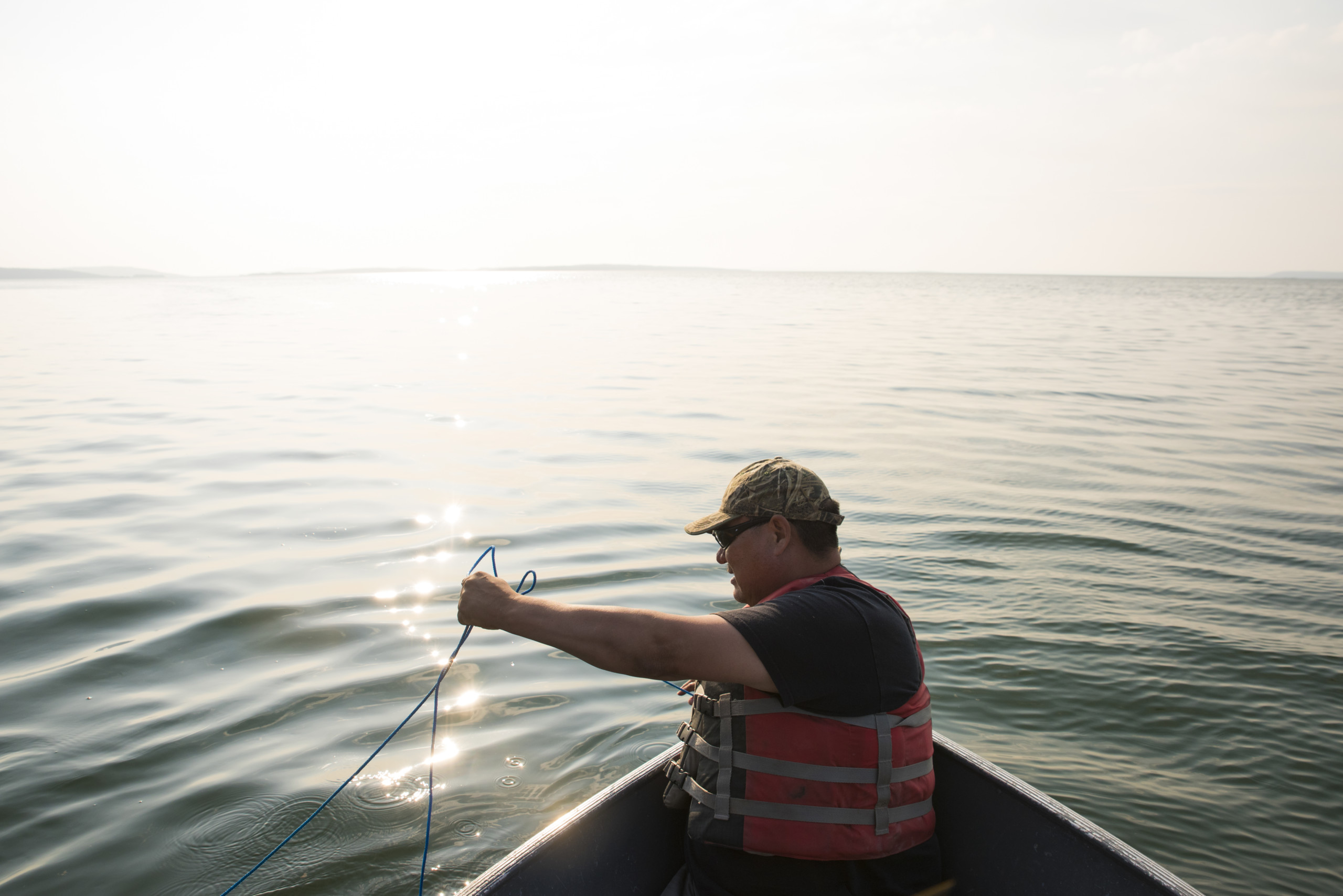 A man on a small fishing boat on calm water. The sun glows brilliantly, so the water reflects gold as well, blending with the sunlight at the horizon