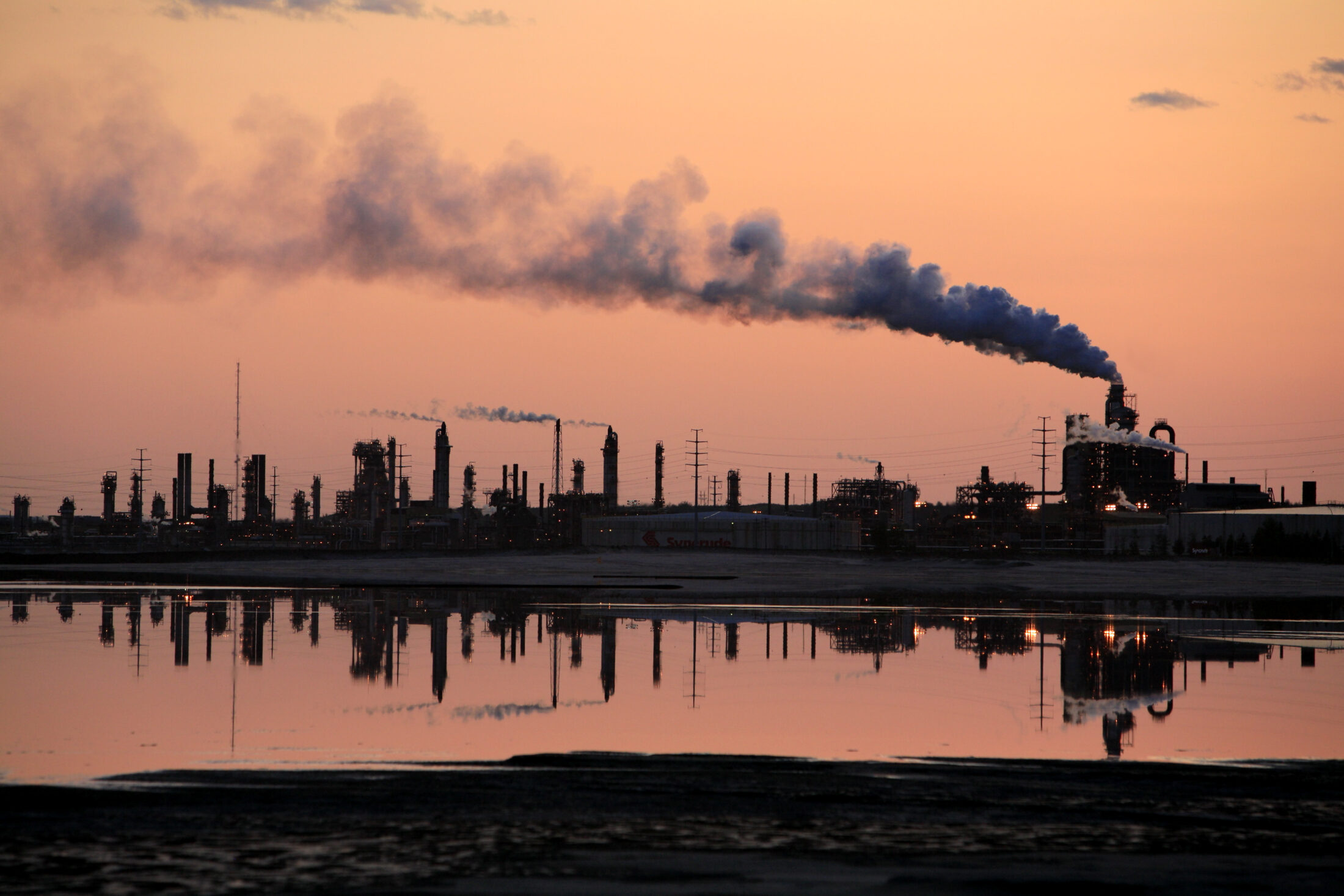 silhouette of Syncrude plant against orange sky, reflected in water of tailings pond