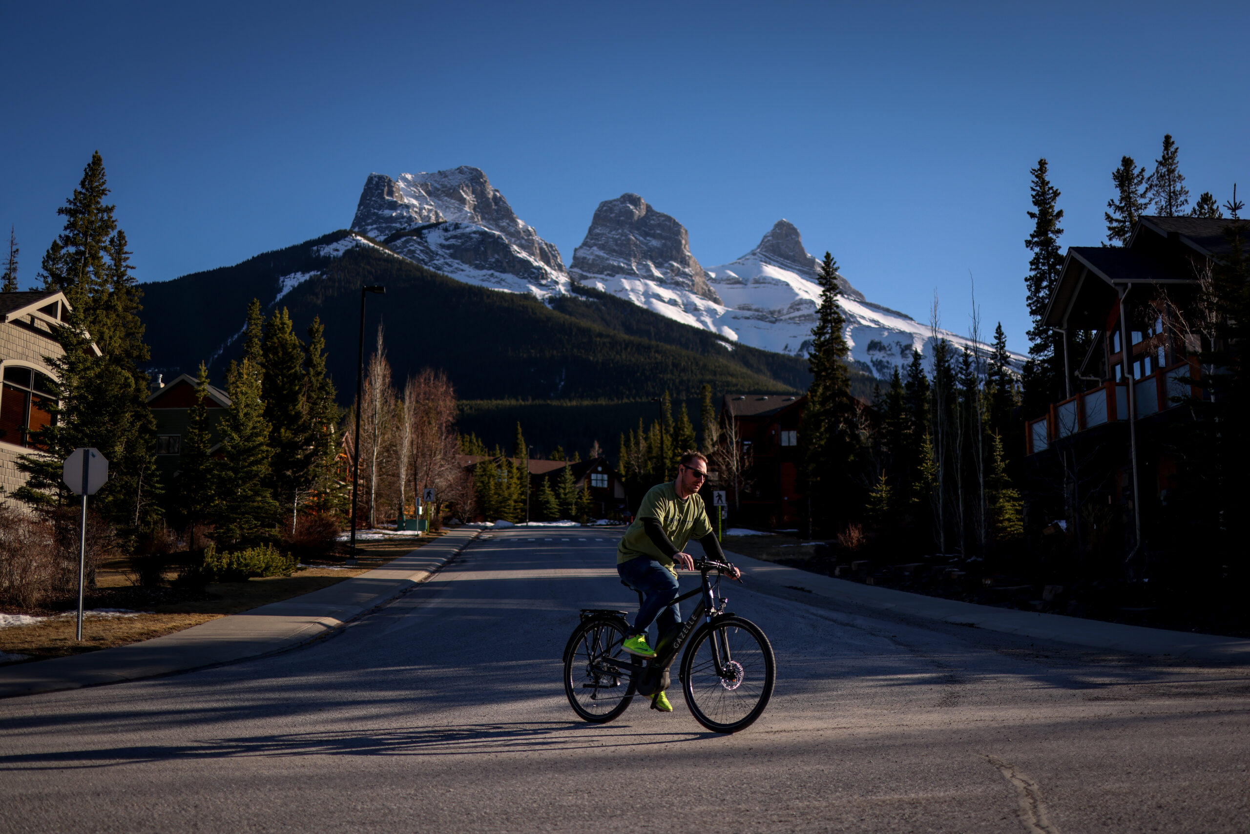 A person biking on a road with the Three Sisters mountain peaks in the background