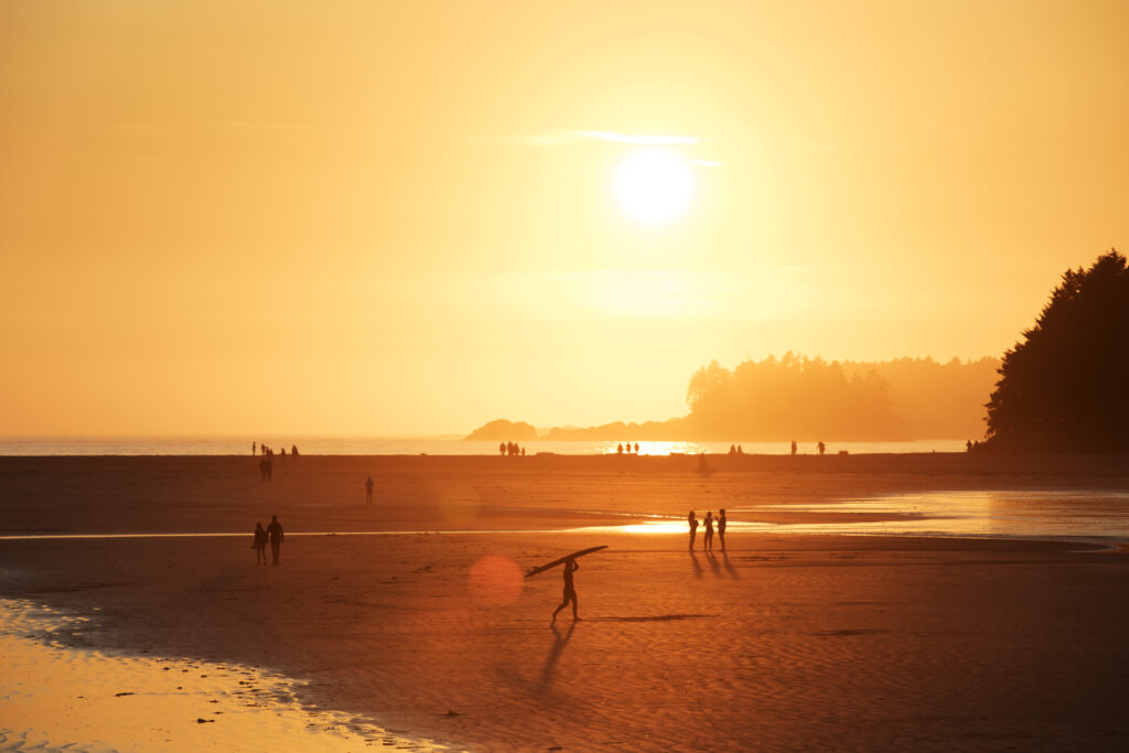 A surfer walks out of the ocean at sunset on Chesterman Beach