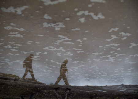the image of two men are reflected in muddy water