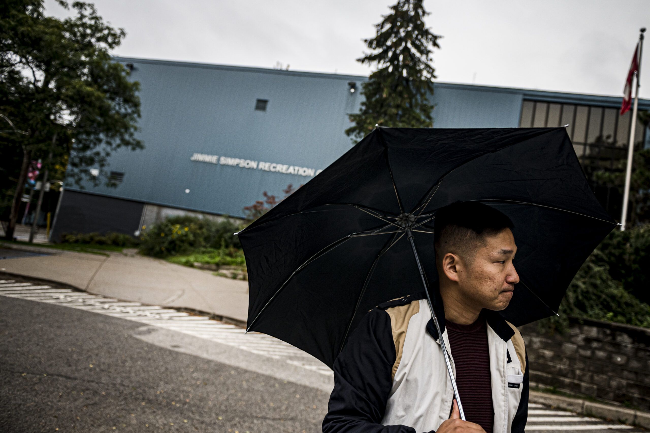 Eon Song walks past the Jimmie Simpson Recreation Centre holding an umbrella
