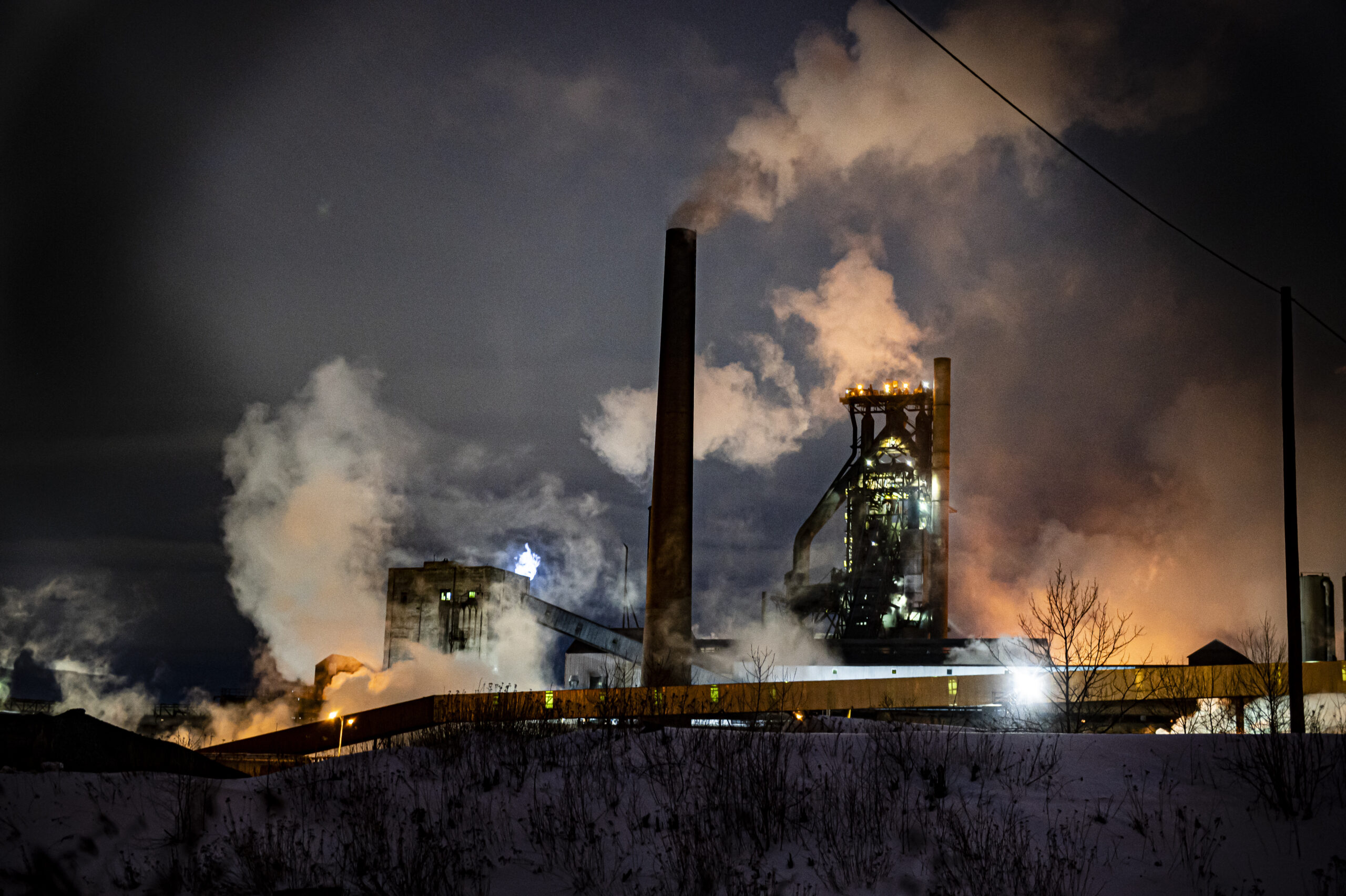 Steam rises from the industrial machinery of the Algoma Steel plant at night. 