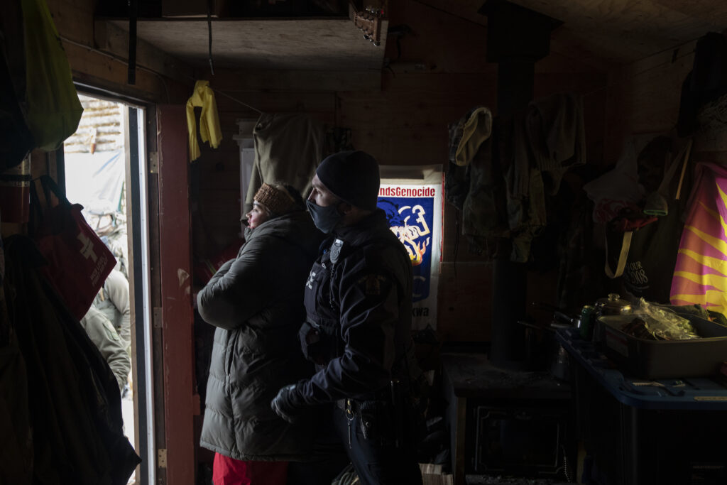 An RCMP officer arrests Snaylynne Sampson in a wooden tiny house