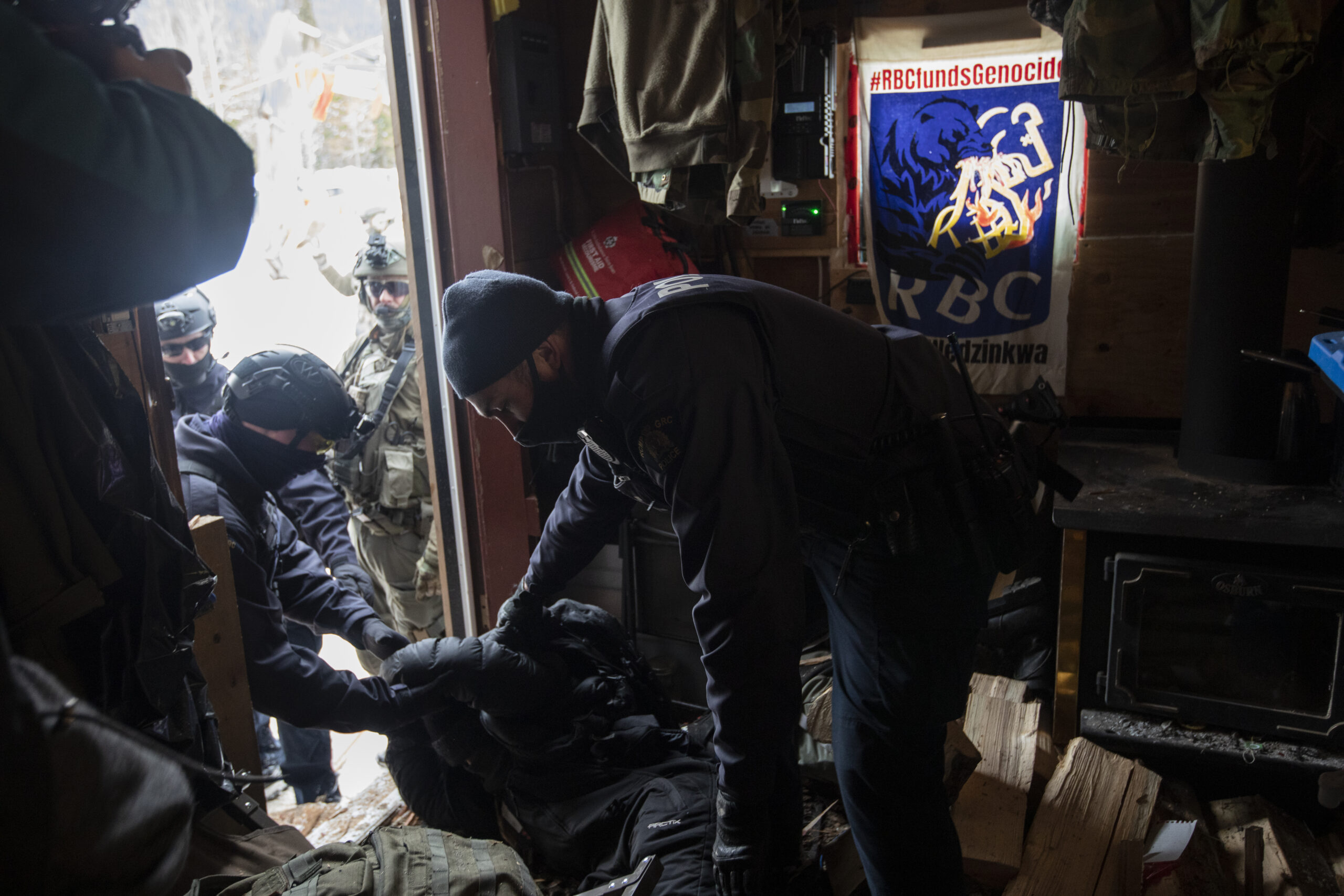 RCMP officers lean over an individual lying on the ground as they perform arrests in a small one-room wooden structure in Gidimt'en territory