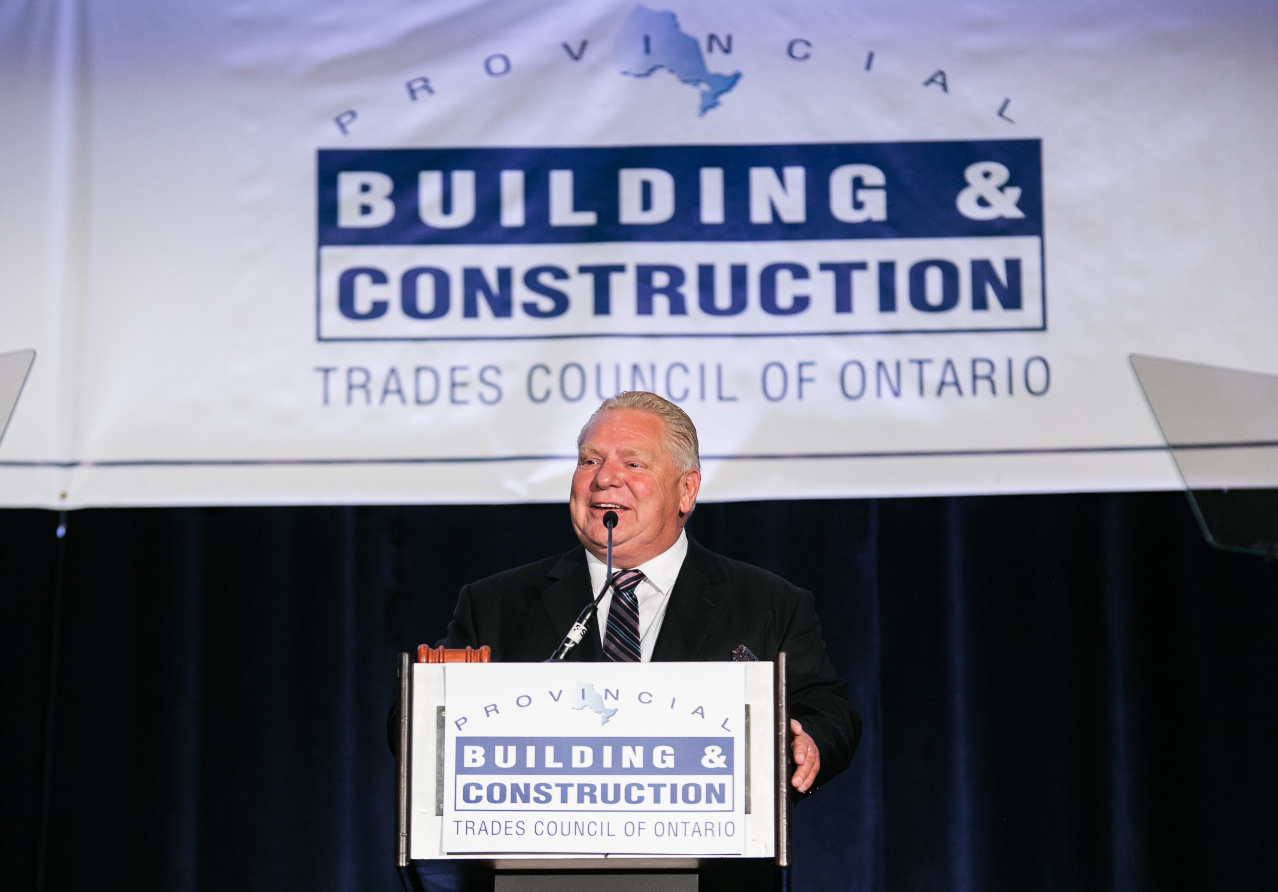 Premier Doug Ford smiles as he speaks at a podium for a building and construction industry event. 