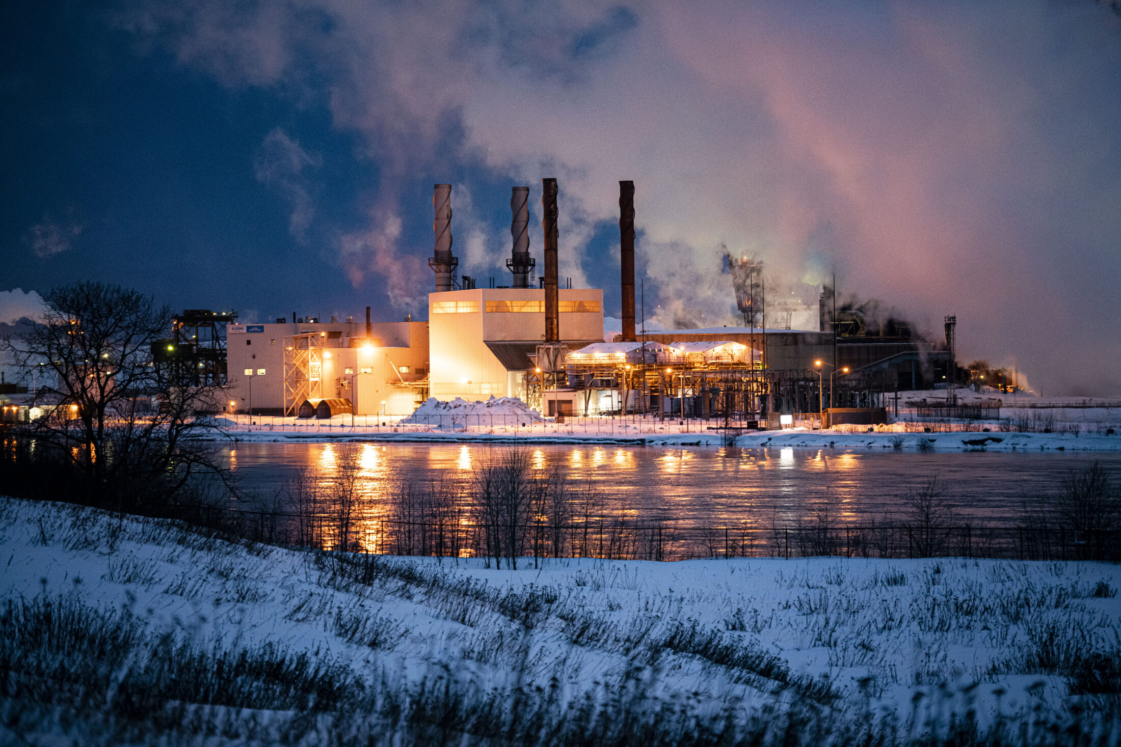 Steam rises from the Algoma Steel plant in Sault Ste. Marie, Ont., seen at night from across a river as snow blankets the ground. 