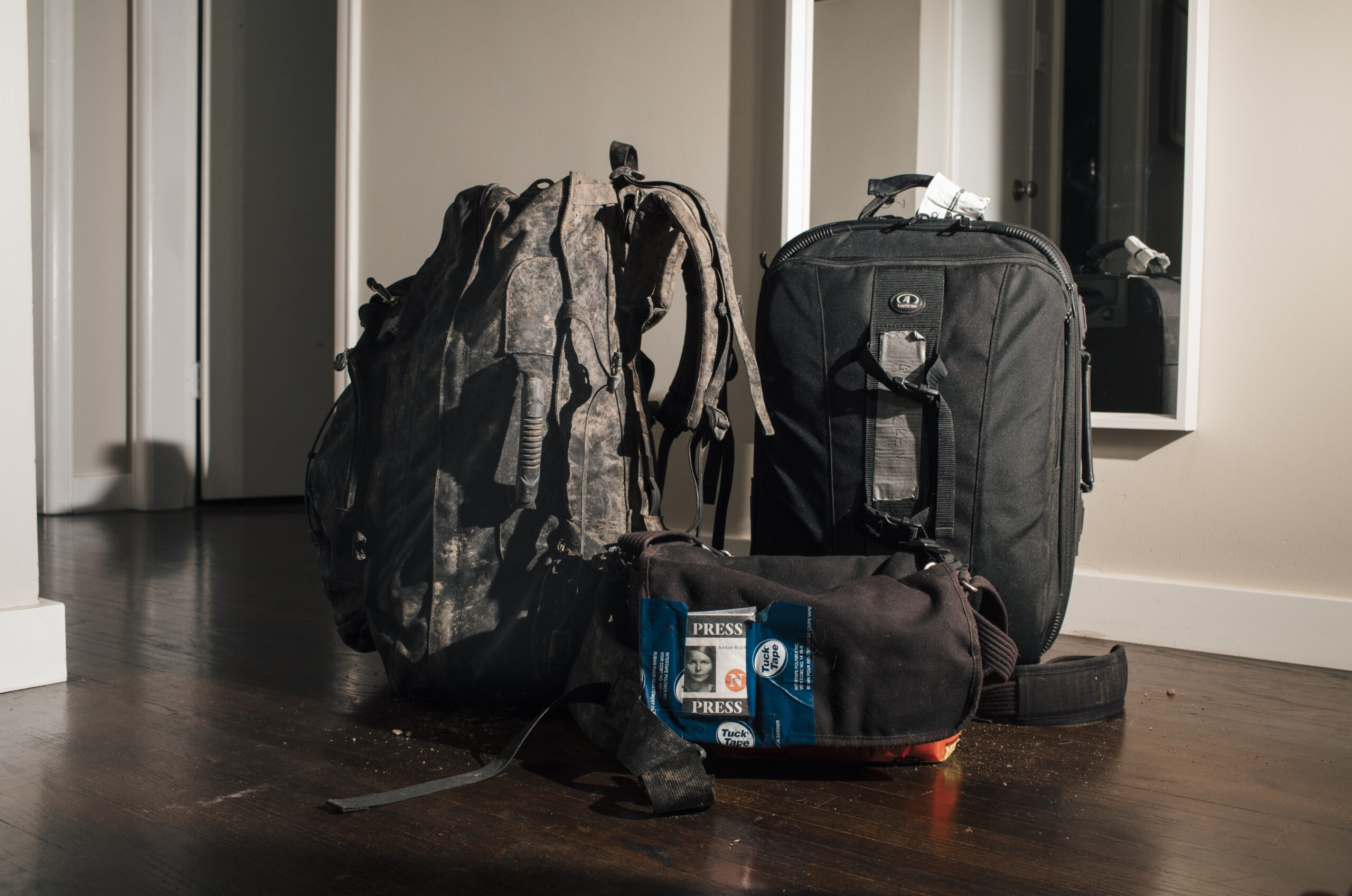 Black backpacks and a bag sit on a wooden floor