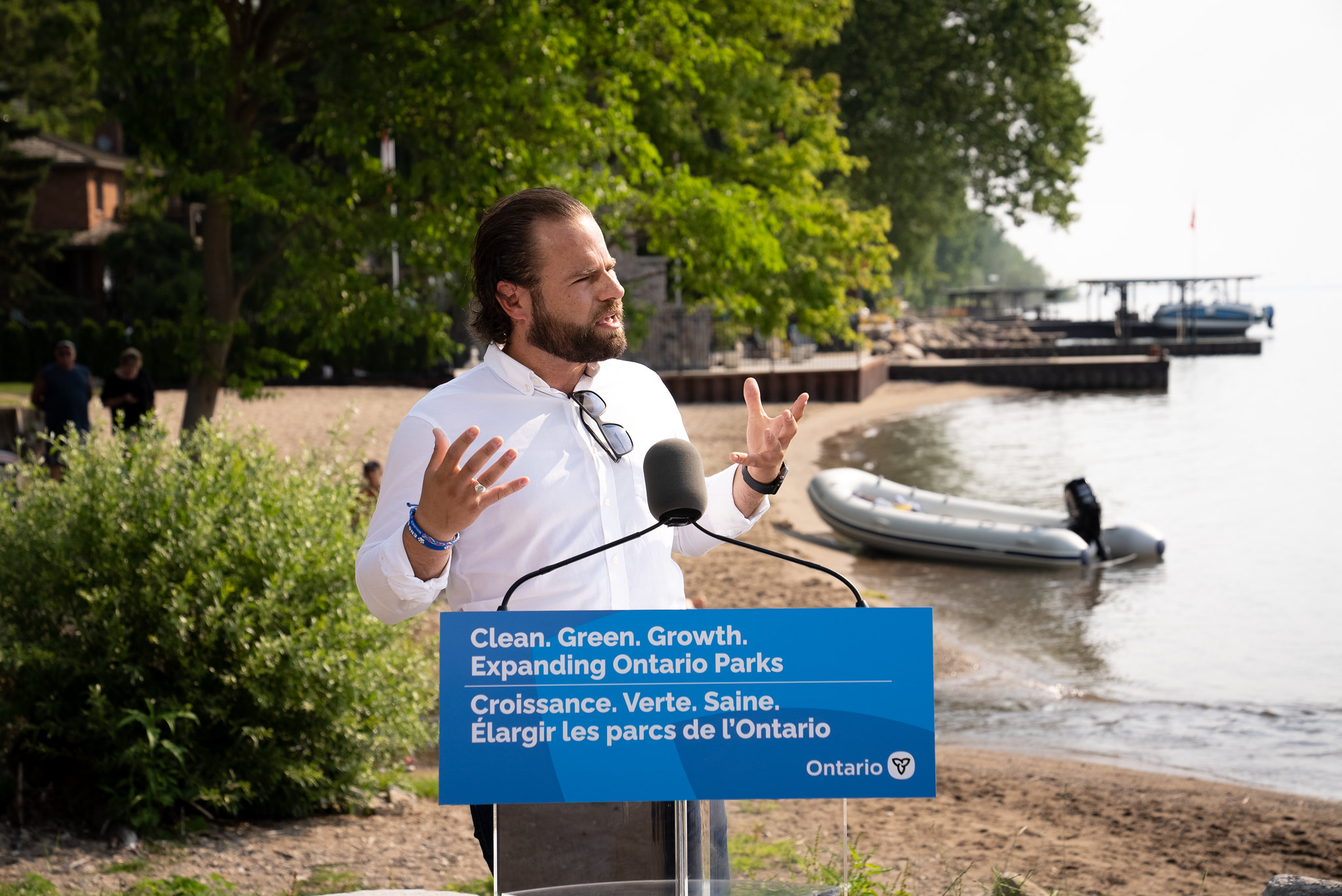David Piccini speaks at a podium with a beach, boats and lush trees in the background. 