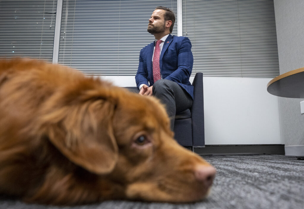 Ontario Environment Minister David Piccini sits in a chair with his dog Max laying at his feet.