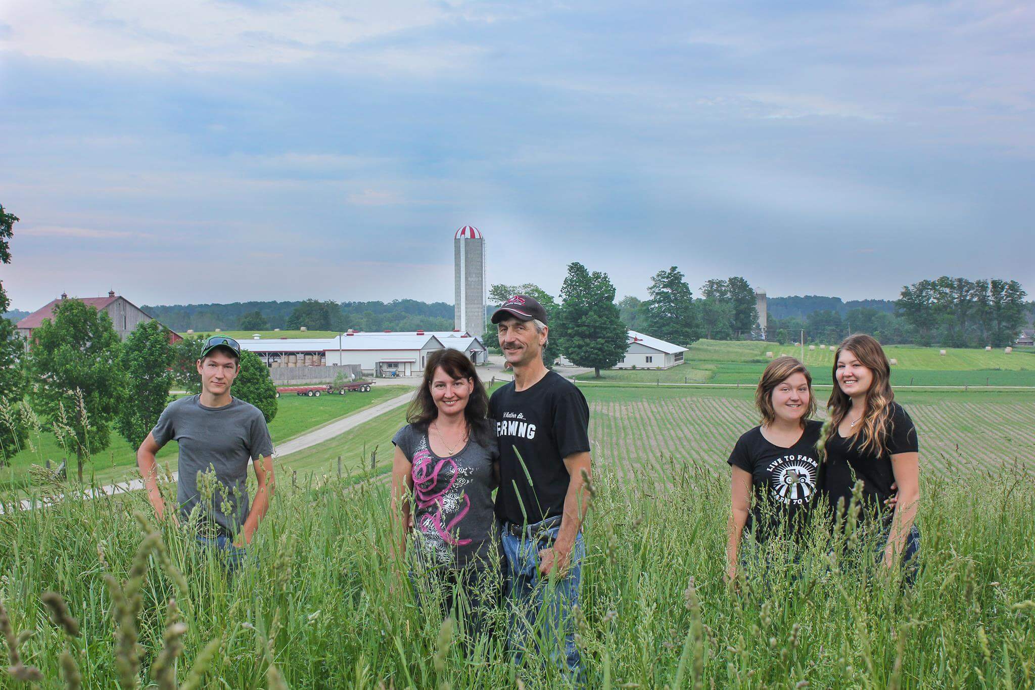 A photo of Michelle Stein and her family, standing in tall grass in front of their farm in South Bruce, Ont.
