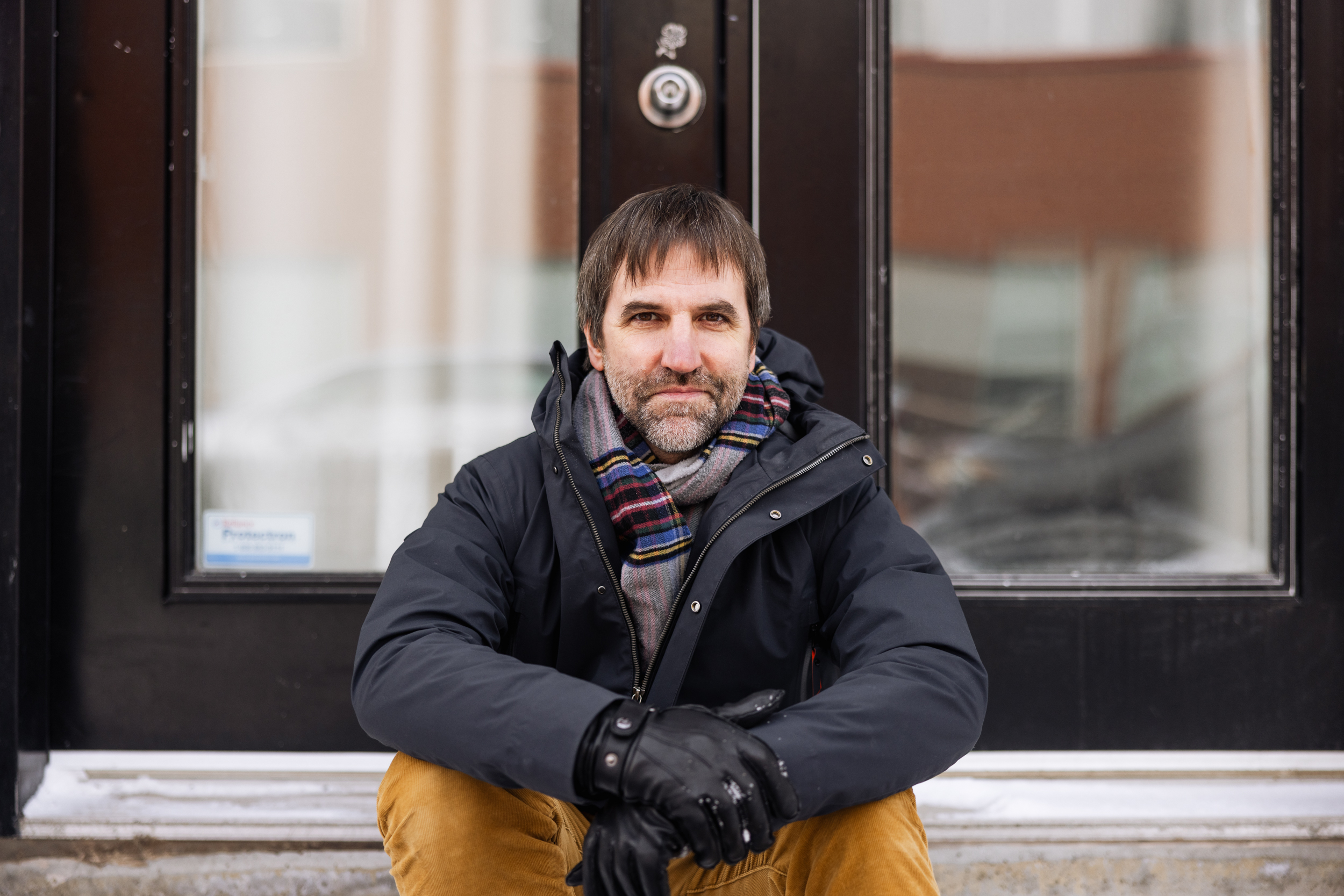 Environment minister Steven Guilbeault, in winter clothes, sits on a stoop.