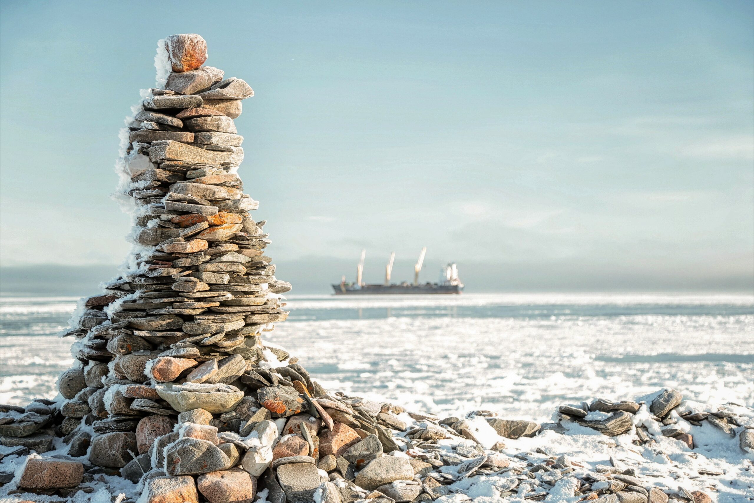 Inuksuk on shore in the foreground as a supply ship moors of the coast of Arviat, Nunavut