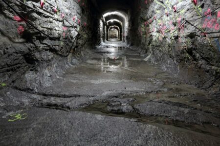 Colourful paint markings on the rocky walls of a tunnel, with water puddling on the bottom.