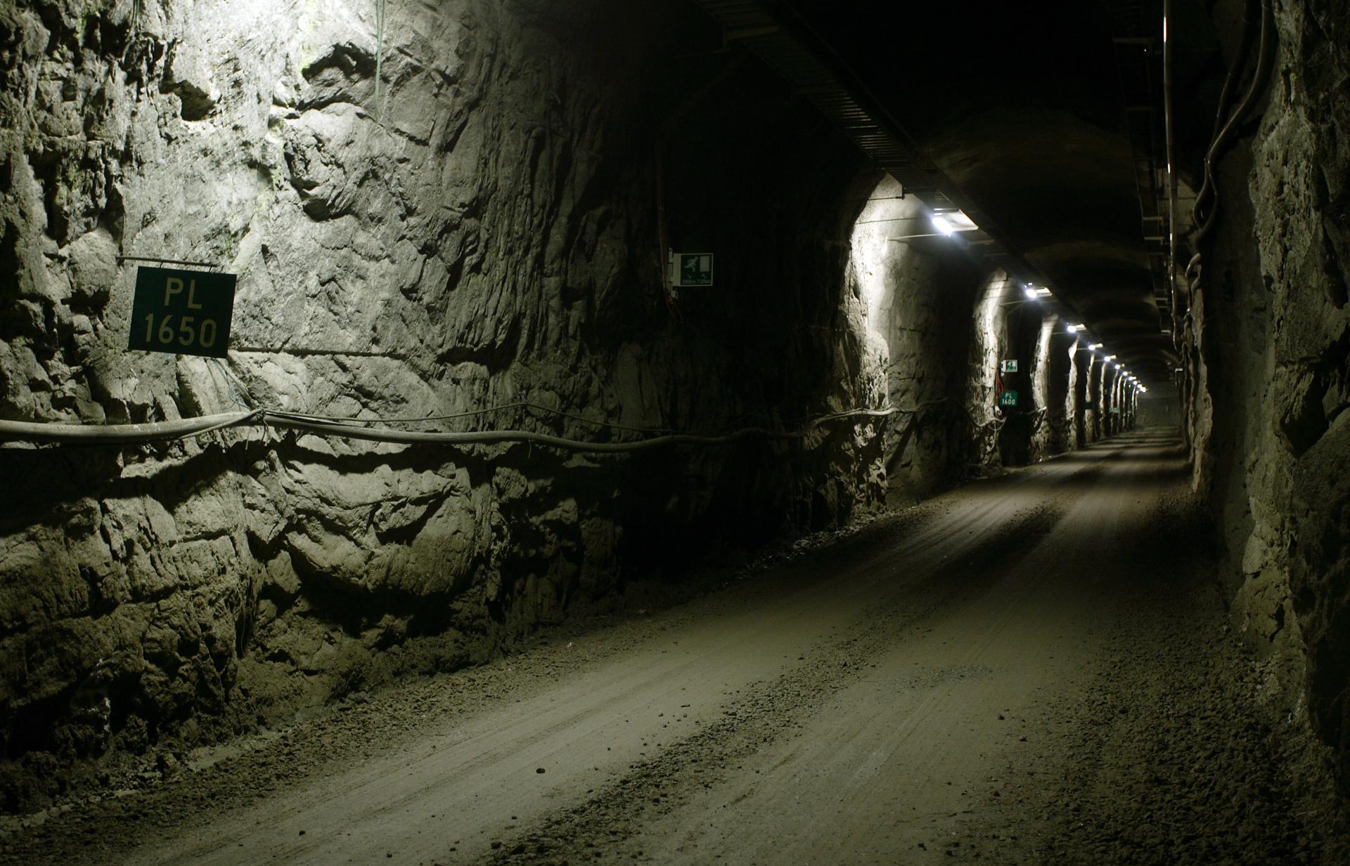 A long view of an empty tunnel with rocky walls and overhead lights leading in the distance.