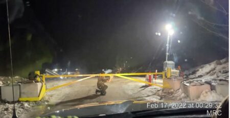 A grainy dashcam image shows a person using a hand-held tool to drill through a big yellow gate