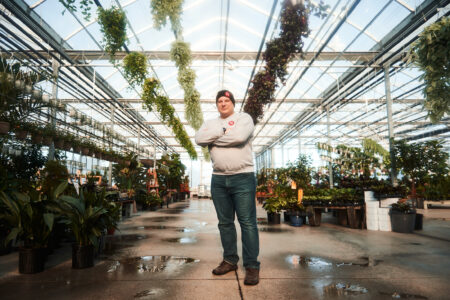 Reporter Carl Meyer is seen wearing Narwhal gear, with his arms crossed, standing in a greenhouse.