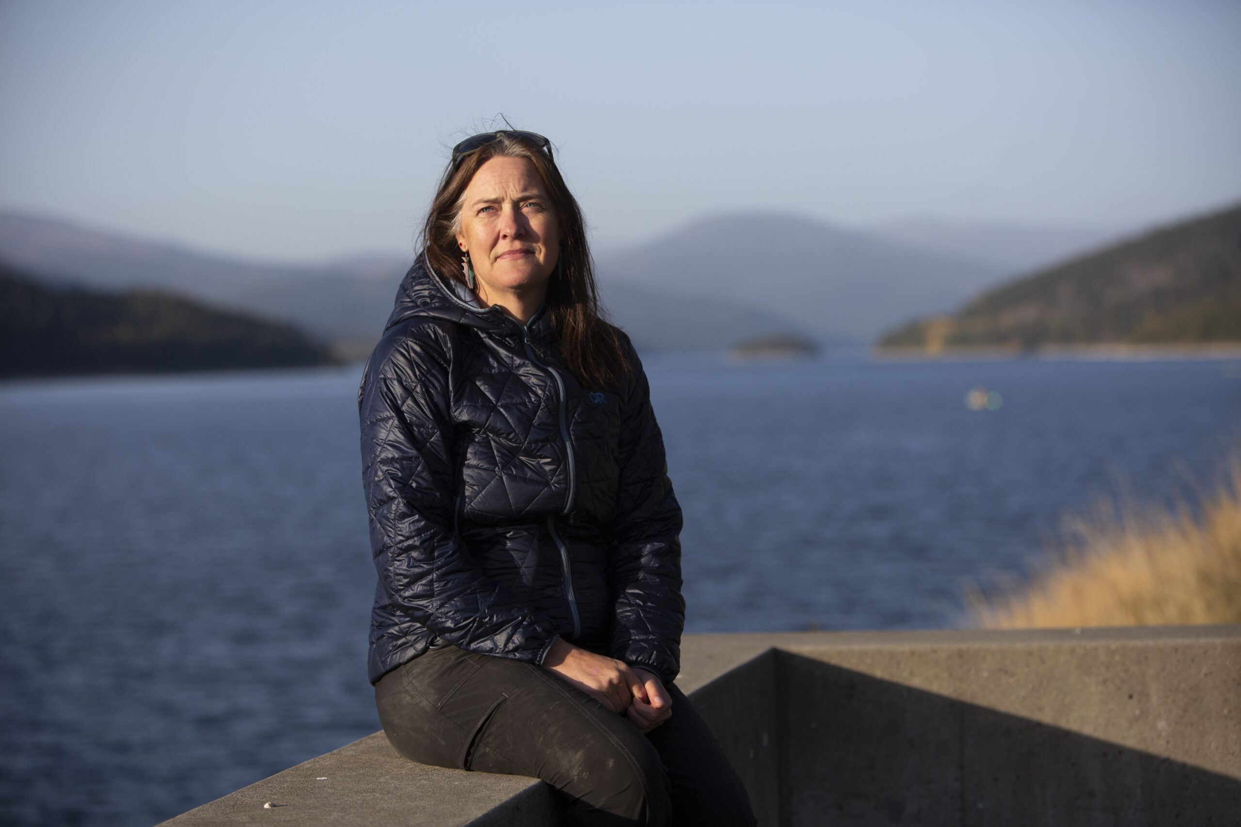 Senior research scientist Erin Sexton, from the Flathead Lake biological research station at the University of Montana sits on a concrete structure in front of a lake. Sexton wants the International Joint Commission to investigate pollution from B.C. coal mines owned by Teck Resources. 