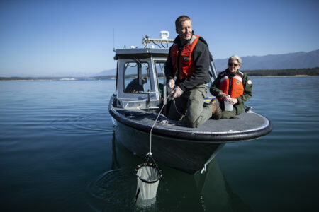 Two men sit on the front of a boat over glassy water on Lake Koocanusa