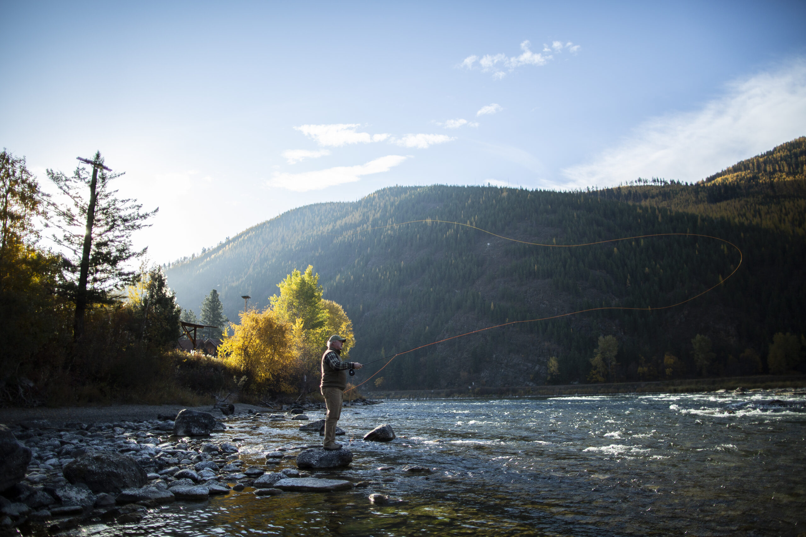 A man stands on a river casting a fly fishing rod