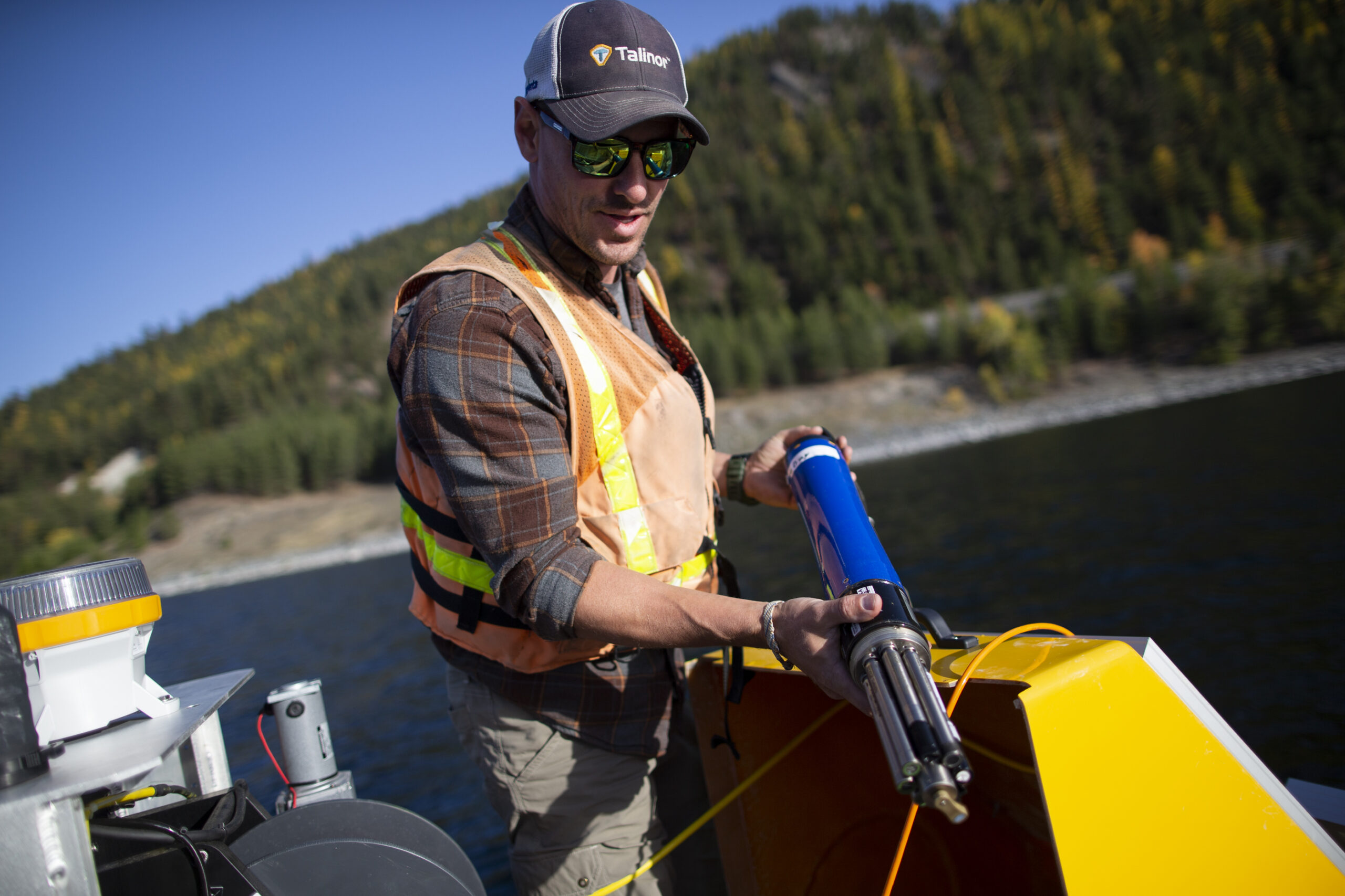 A man in an orange safety vest holds a blue water testing device in a boat