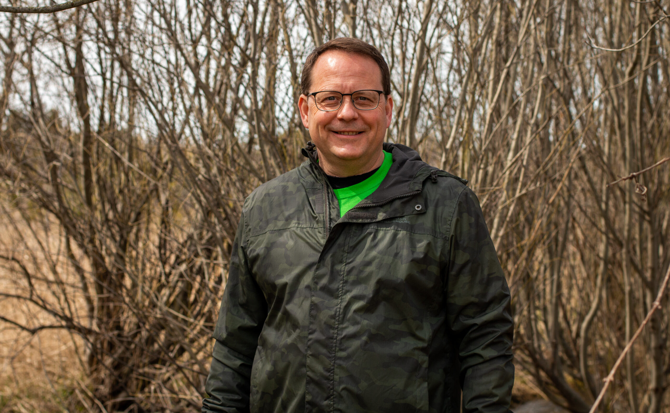 Ontario election 2022: Mike Schreiner smiles facing the camera in front of trees with bare branches.