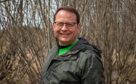 Ontario election 2022 story: Mike Schreiner smiles, standing in front of trees with bare branches.