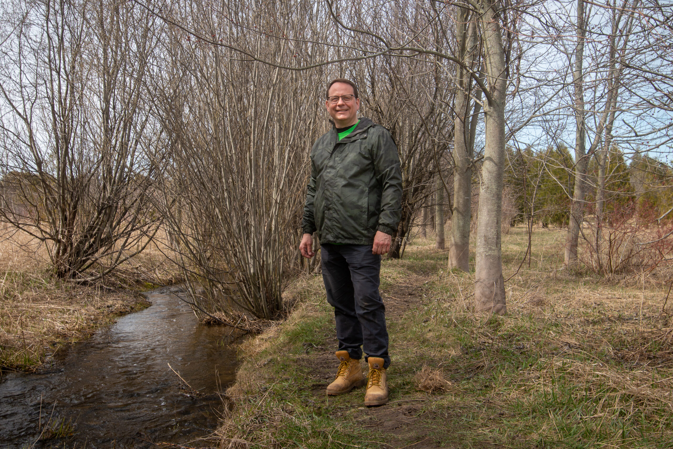 Ontario election 2022: Mike Schreiner wears hiking clothes, standing next to a creek in early spring.