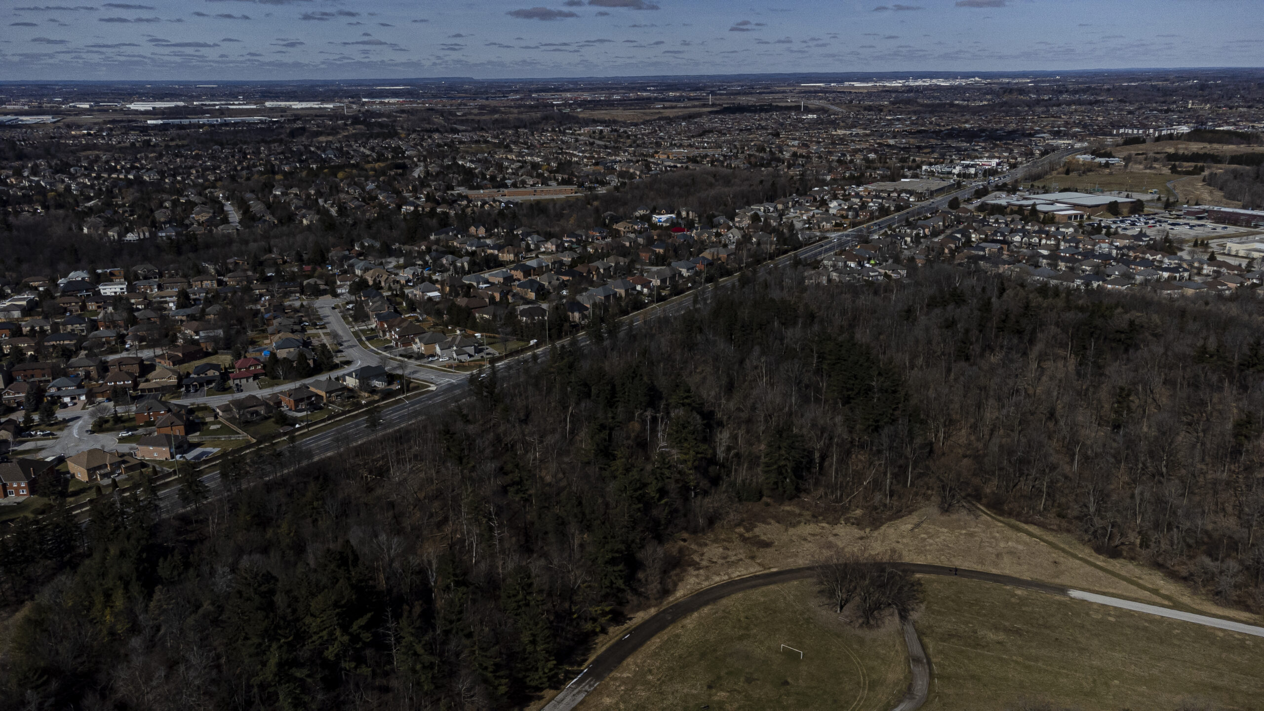 An aerial view of suburban sprawl abutting a highway and a forested area.