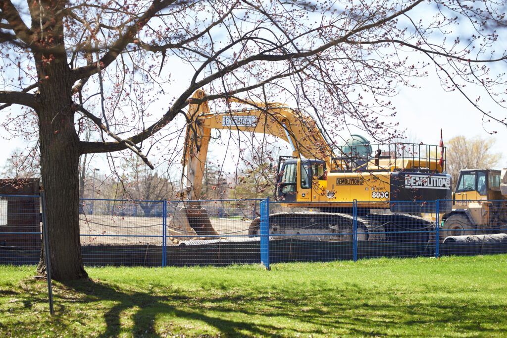 Tree and grass in foreground, backhoe and other construction equipment in background, digging at the site of the new Ottawa Hospital on April 28, 2022