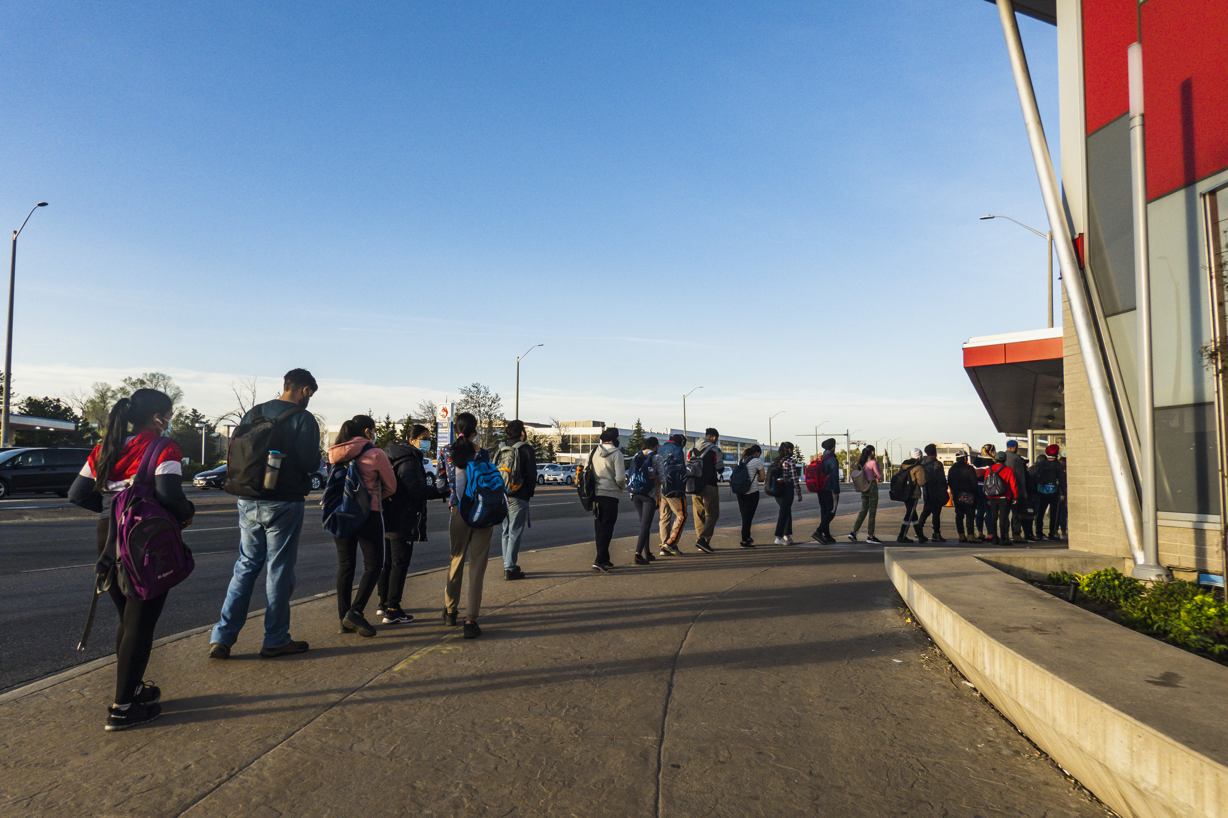 A queue of people wait for a bus.