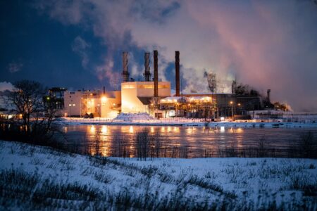 Steam rises from the Algoma Steel plant in Sault Ste. Marie, Ont., seen at night from across a river as snow blankets the ground.