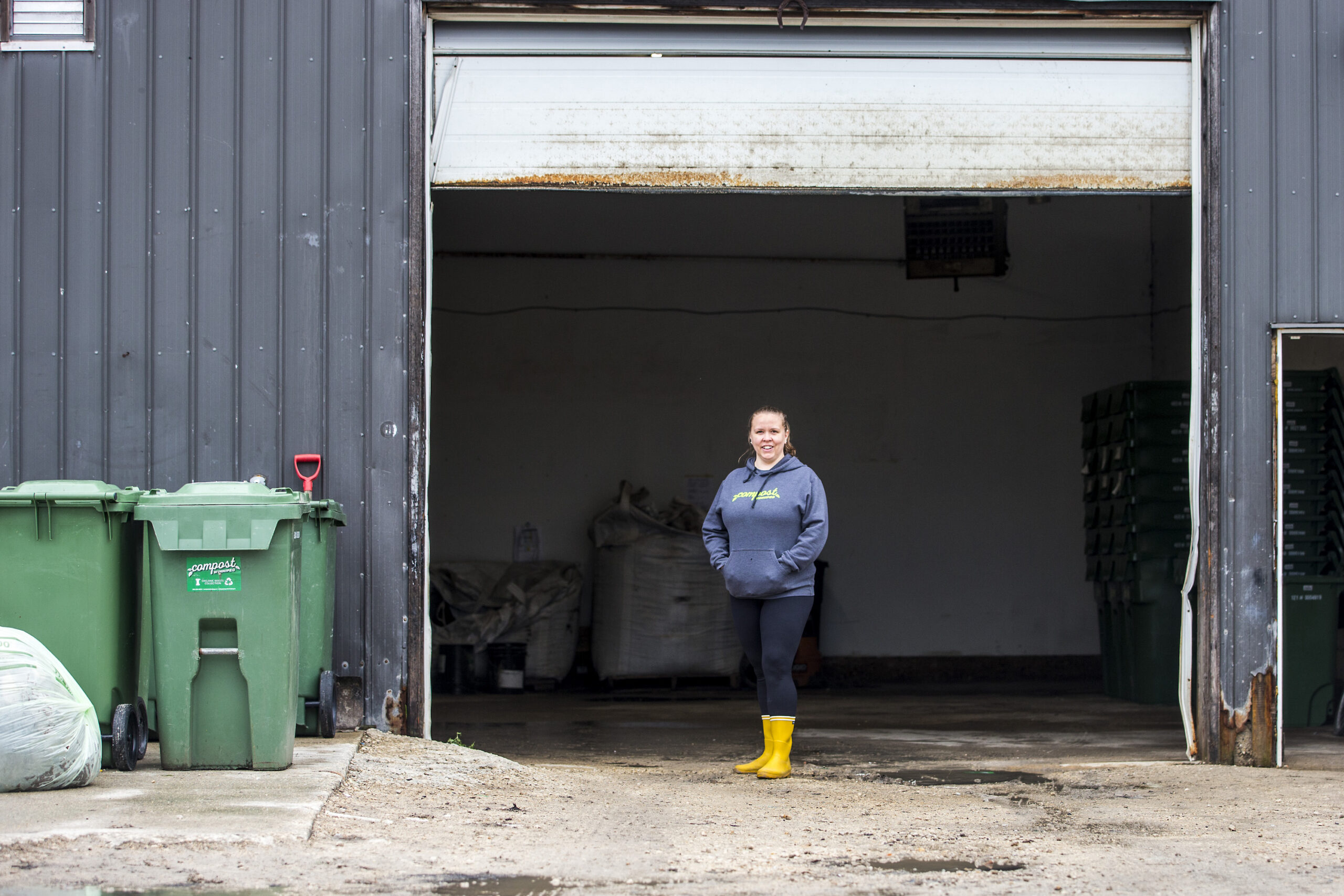 Karrie Blackburn stands in front of an open garage door at Compost Winnipeg headquarters