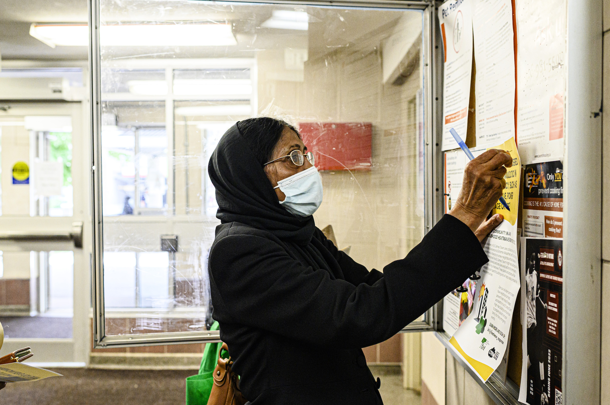 Shaheen Kausar, resident of St. James Town and volunteer with Community Resilience to Extreme Weather (CREW), posts a bulletin in a residential building lobby, in St. James Town.
