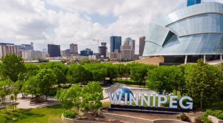 green trees near city buildings and sign that reads Winnipeg during daytime