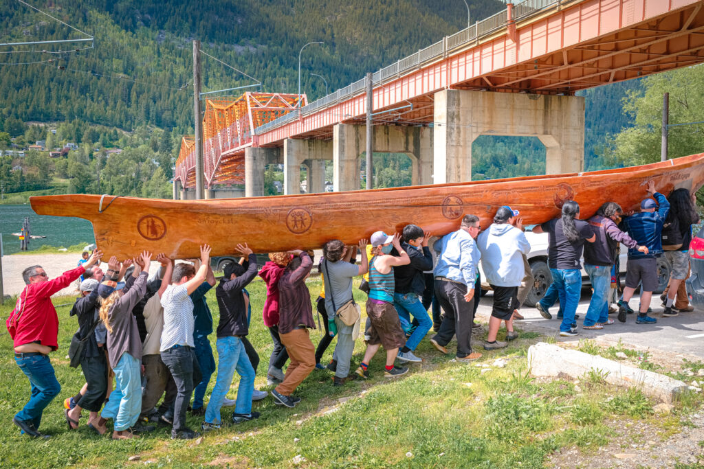 30 people lift the cedar dugout canoe that's being used for the Sinixt journey.