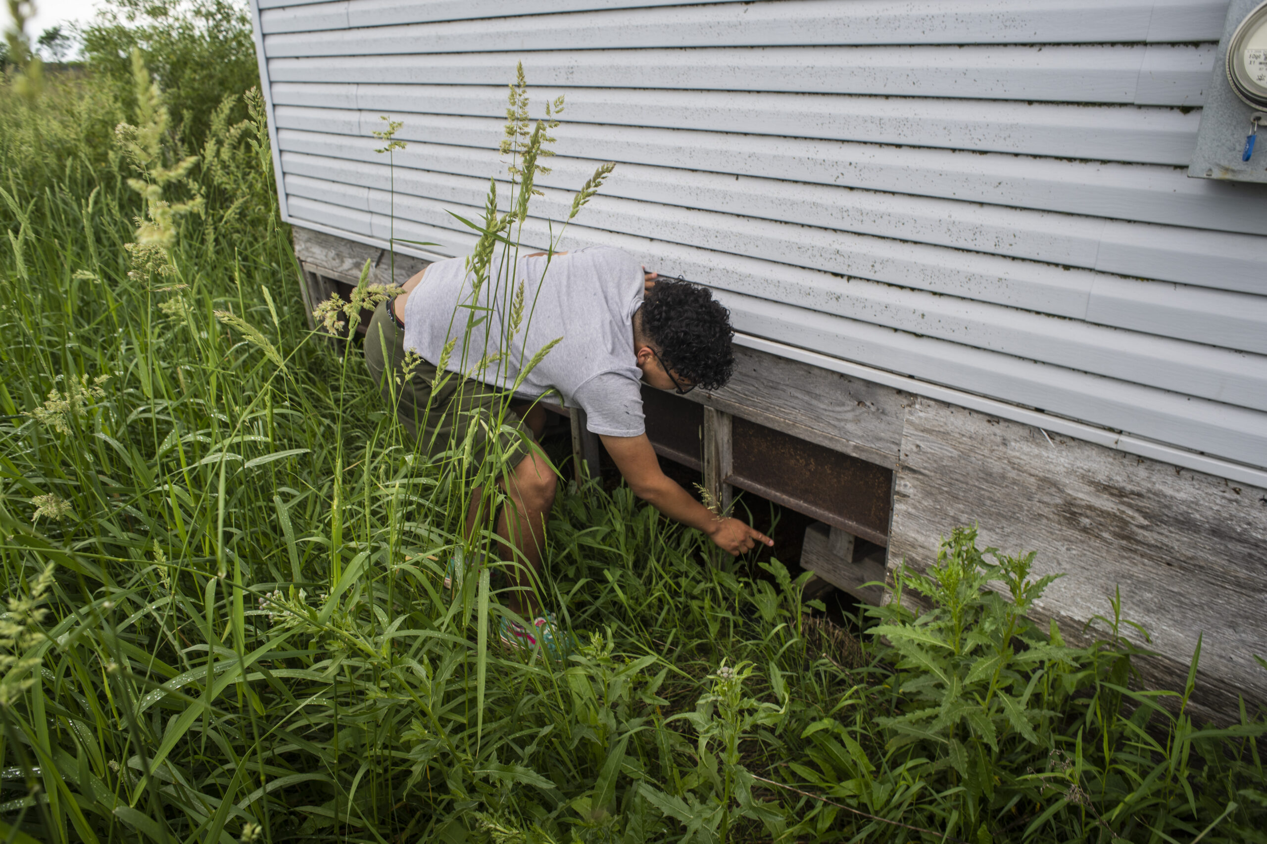 A young man in a grey shirt points under the wooden foundation of a house in Peguis after the flood