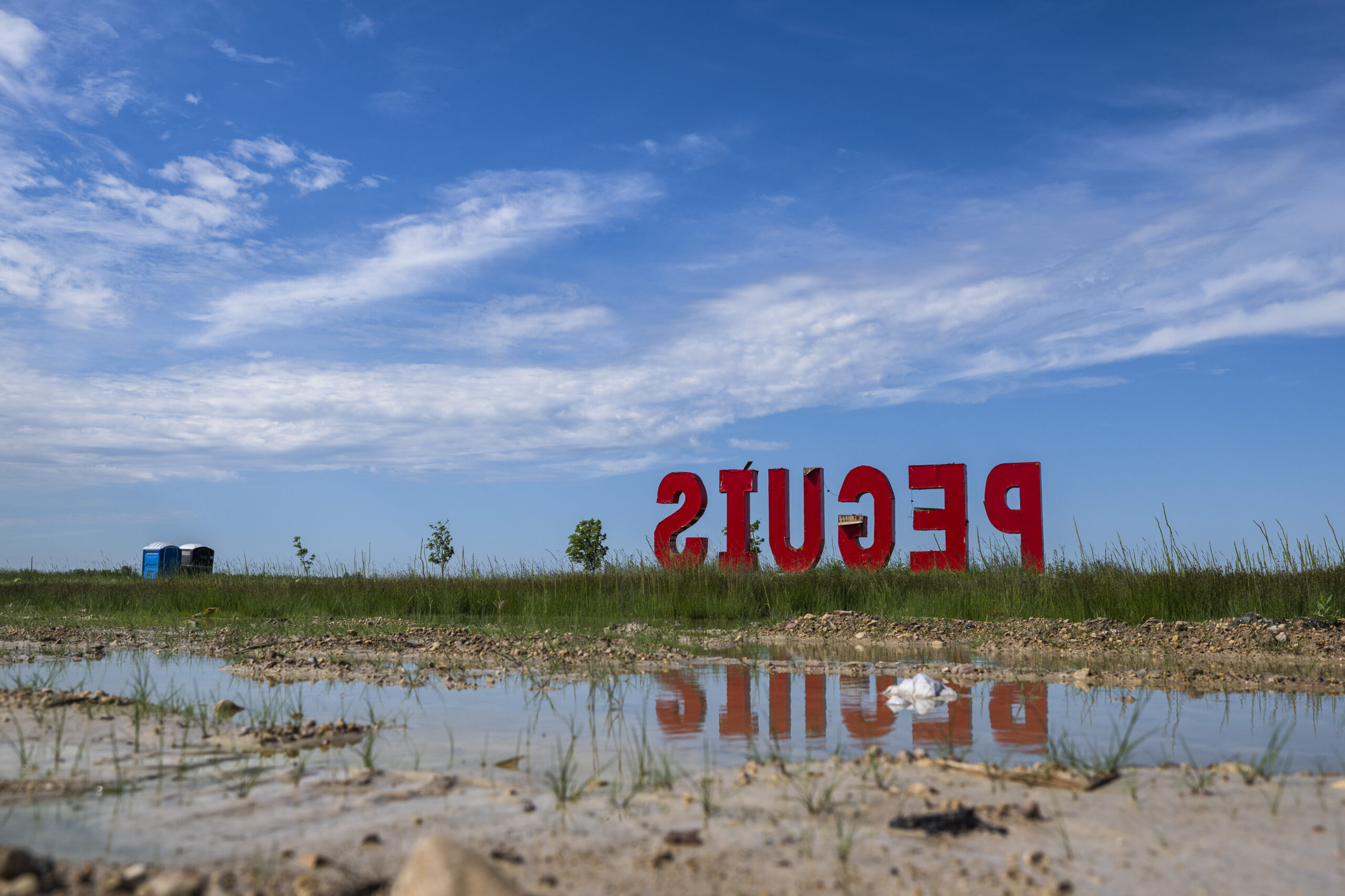 Tall red letters spell Peguis against a blue sky. Shot from behind the sign so the word appears in reverse