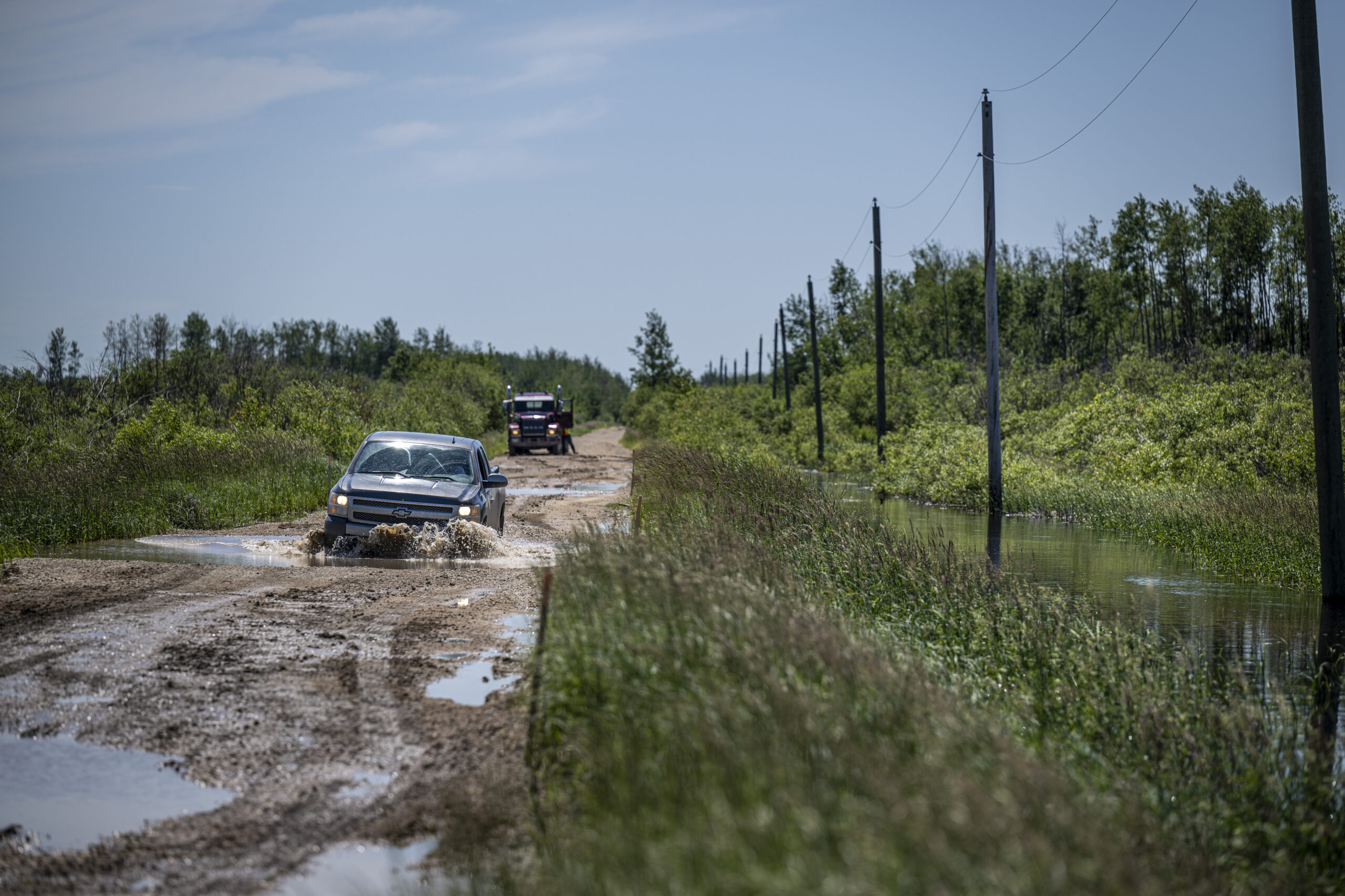 A black truck drives through a deep puddle on a gravel road