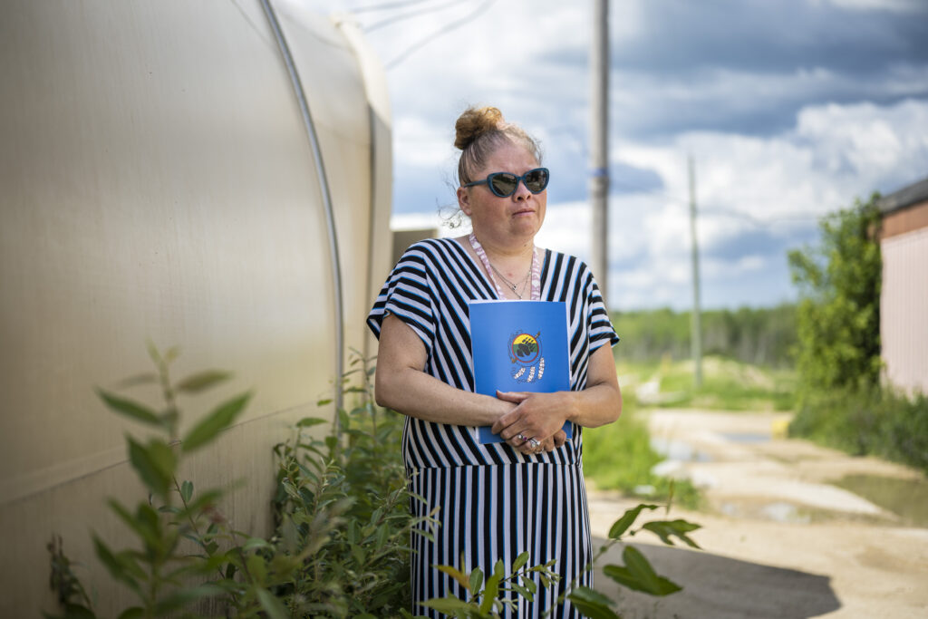 A woman wearing sunglasses and a striped dress holds a blue book close to her chest at Peguis flood emergency centre