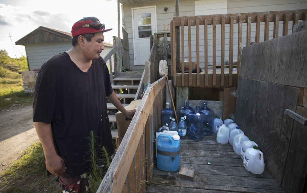 A man in casual clothes looks over a deck railing, where containers of water are lined up