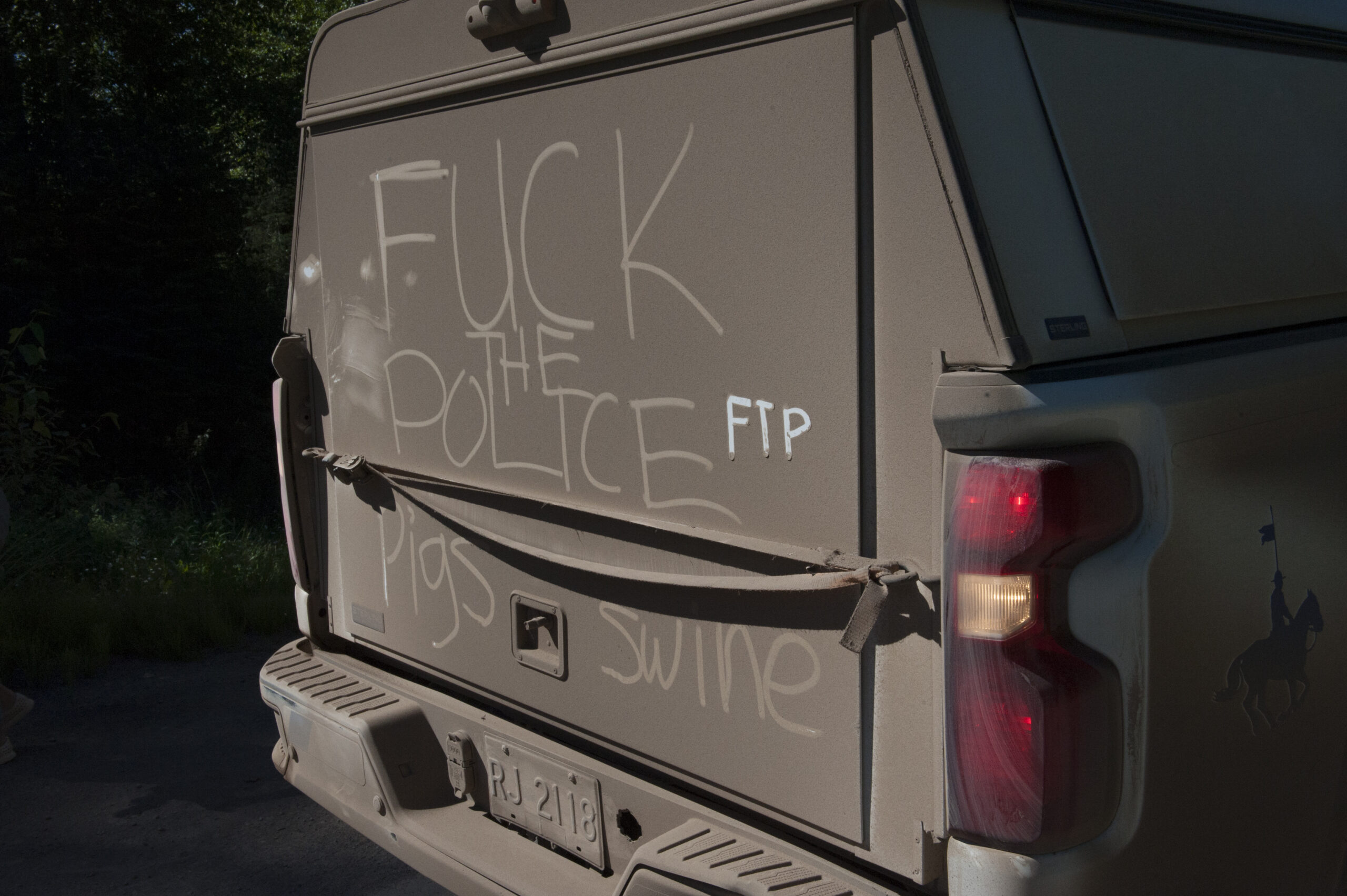 The dirty back of an RCMP truck with "fuck the police" and "pigs swine" written in the dirt