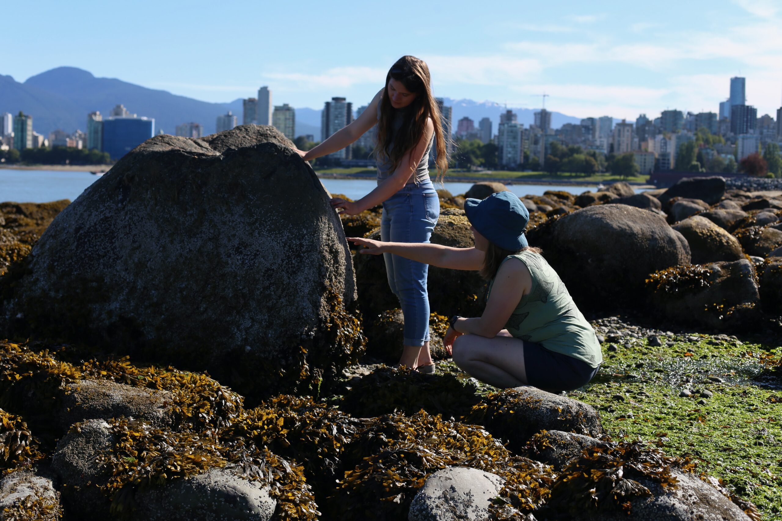 Rebecca Hansen, standing, and Amelia Hesketh, both researchers in Harley's lab at the University of British Columbia, examine marine life on a boulder at Kitsilano Beach during low tide.