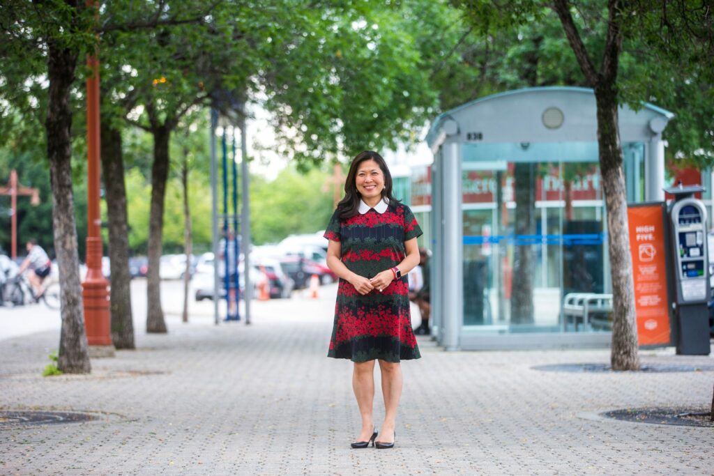 Mary Ng stands near a bus shelter in downtown Winnipeg wearing a patterned dress with a white collar