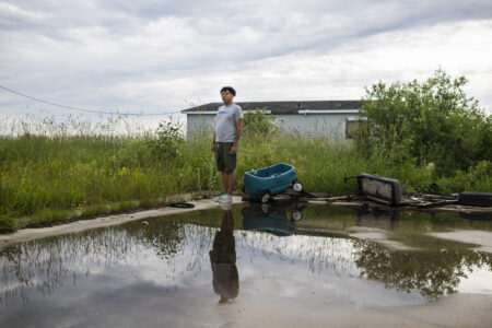 Dysin Spence, who has been living in Winnipeg since 2014, stands in front of his former home in Peguis, with a flooded backyard.