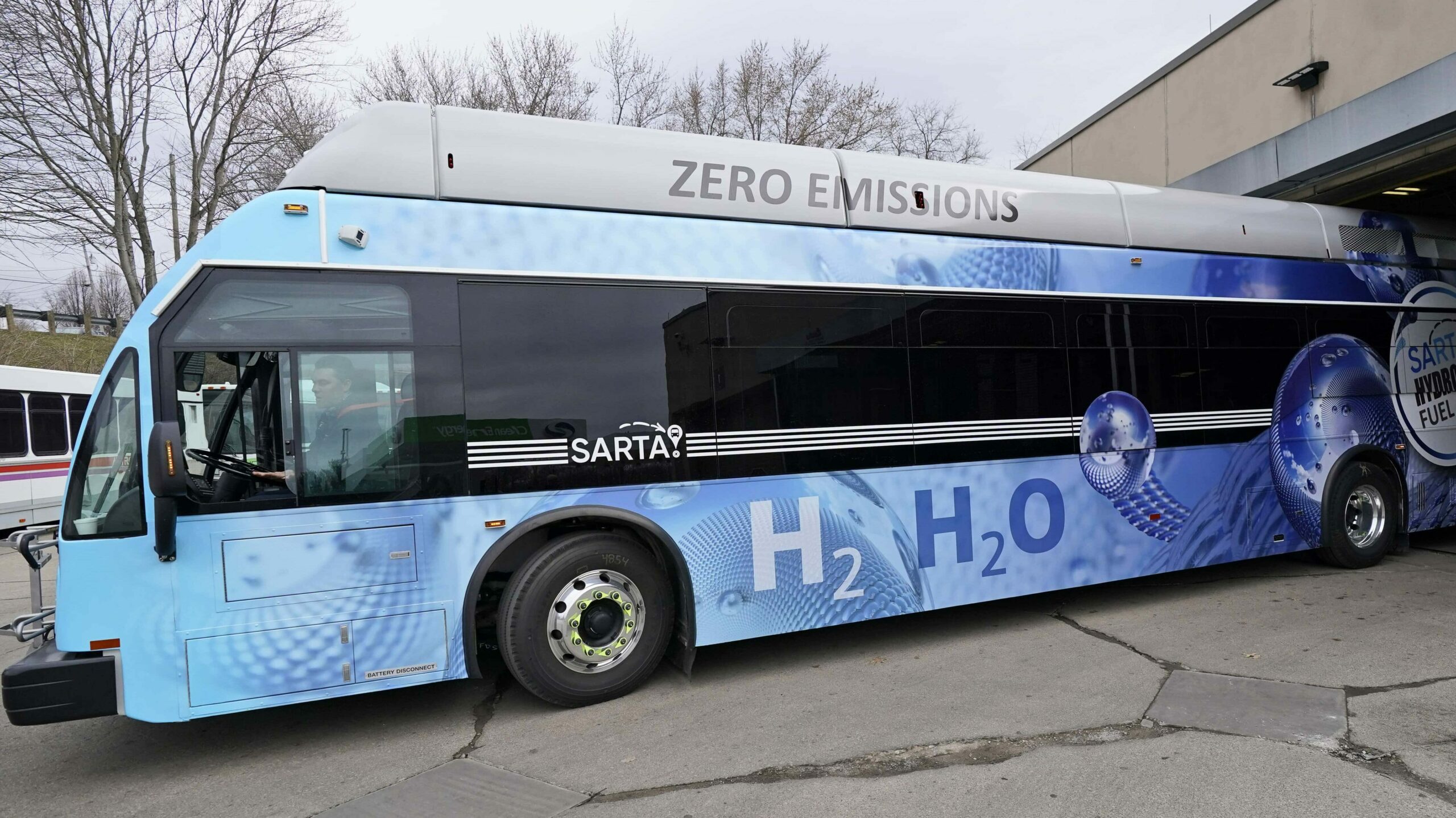 A worker drives a blue hydrogen fuel cell bus out of a terminal in the United States