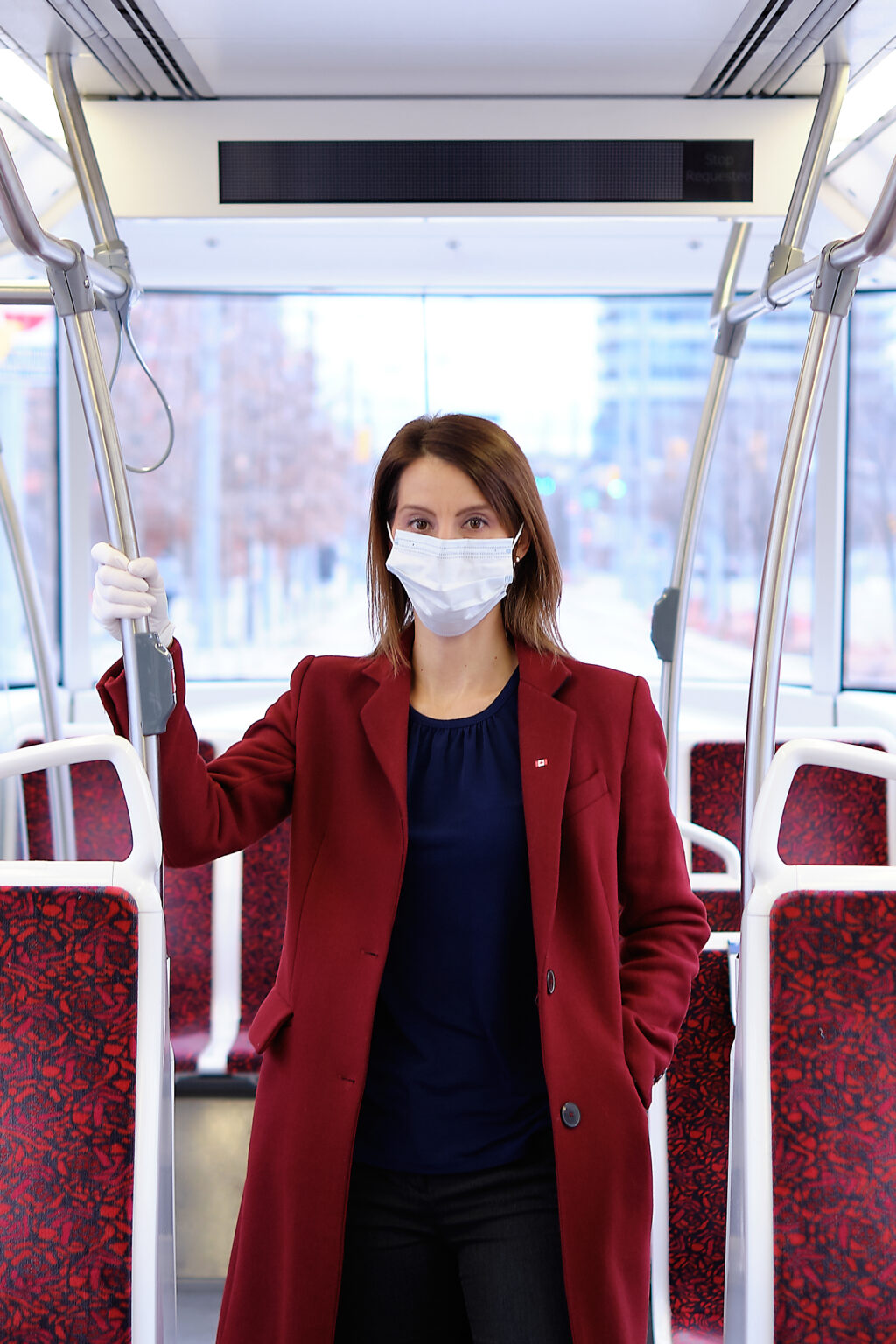 Josipa Petrunic stands inside a transit bus wearing a face mask, a long red coat and a navy shirt