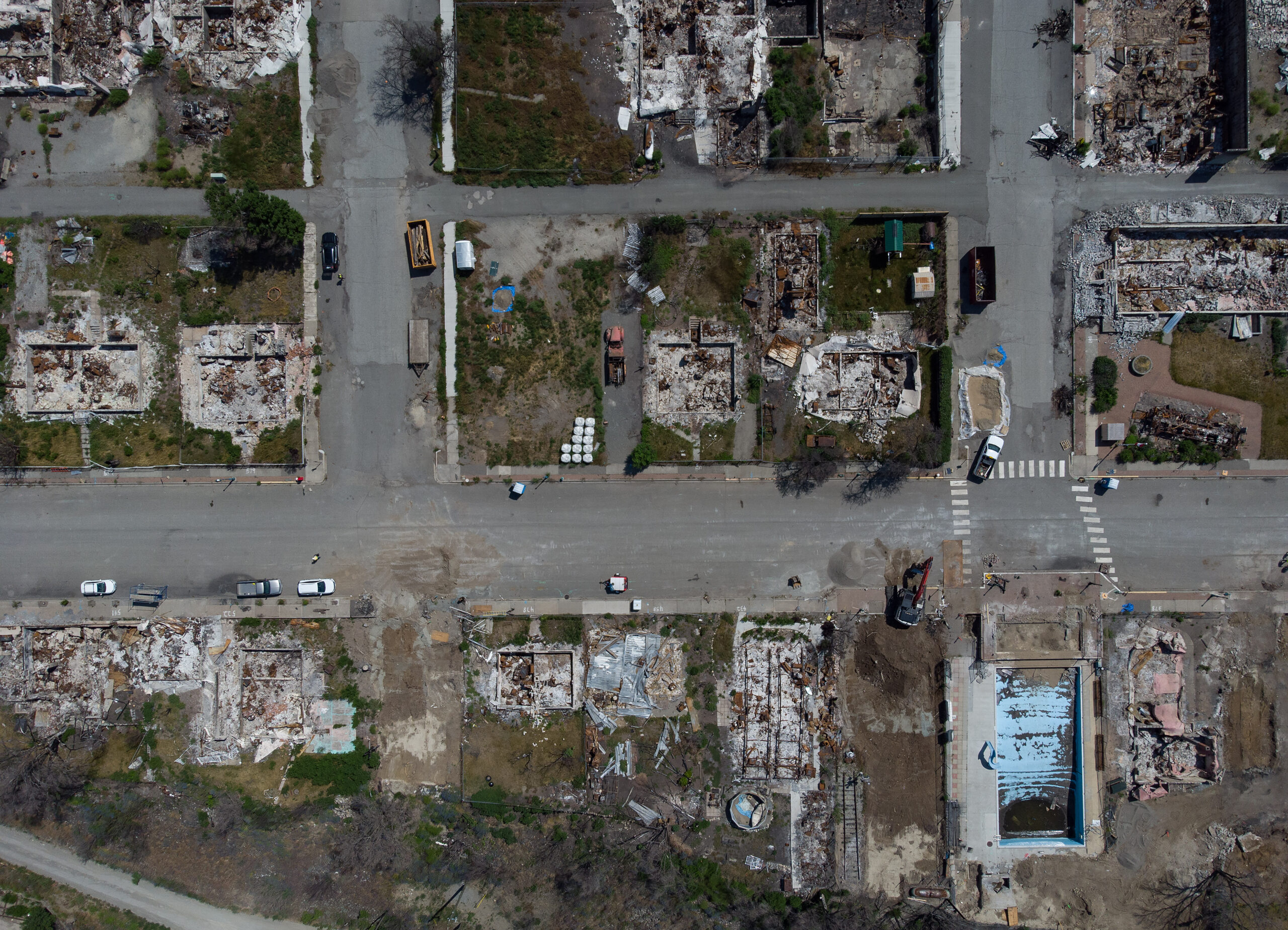 Charred and destroyed houses seen from overhead, with streets, and the remains of a pool can also be seen.