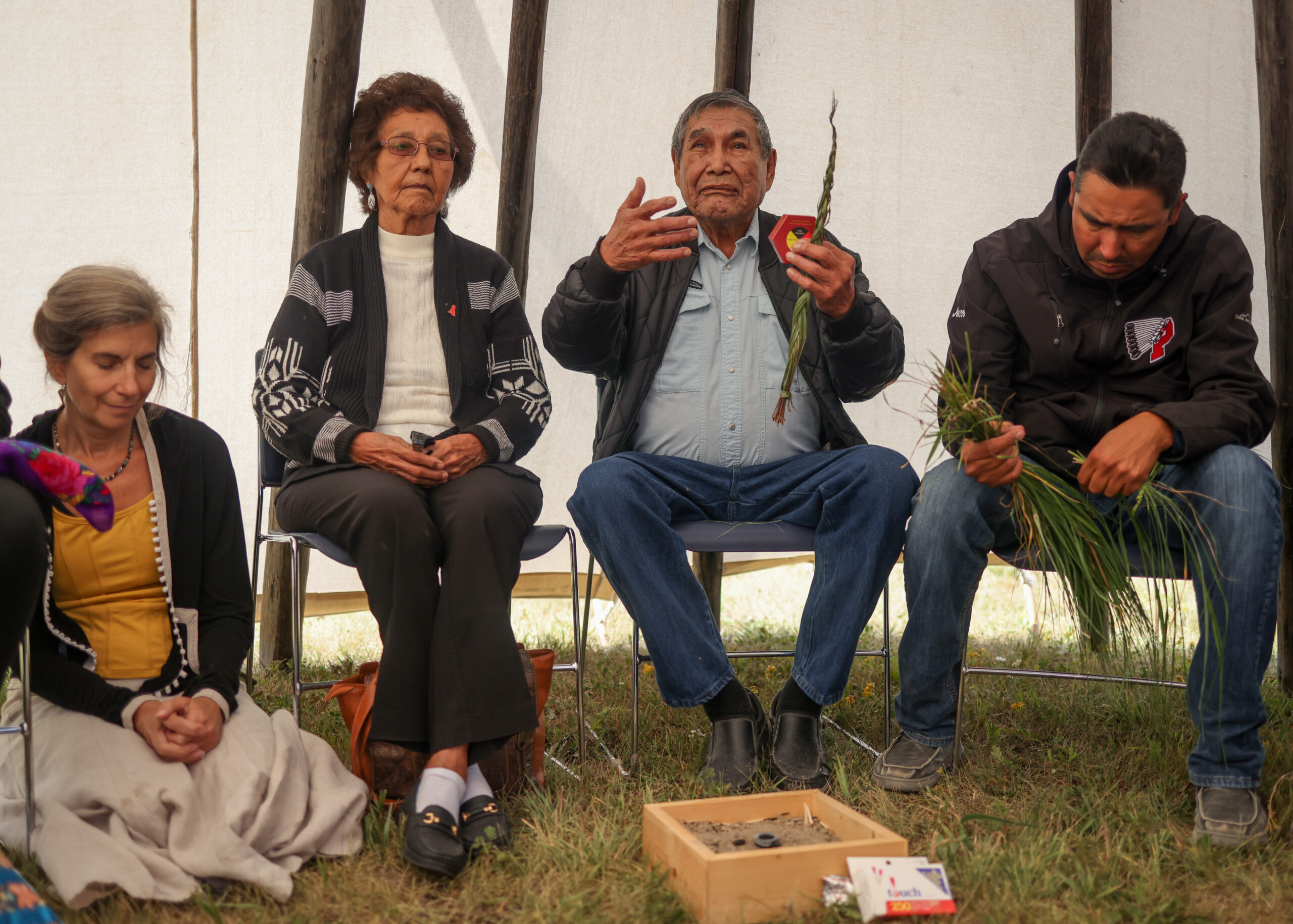 Four people are seated holding sweetgrass at a ceremony on Piikani Nation.